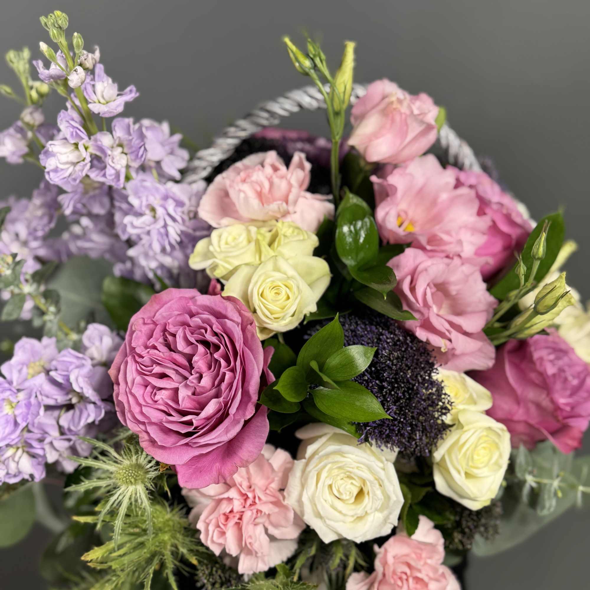 Basket arrangement of pink roses, carnations, lisianthus, cream roses, and lavender stock.