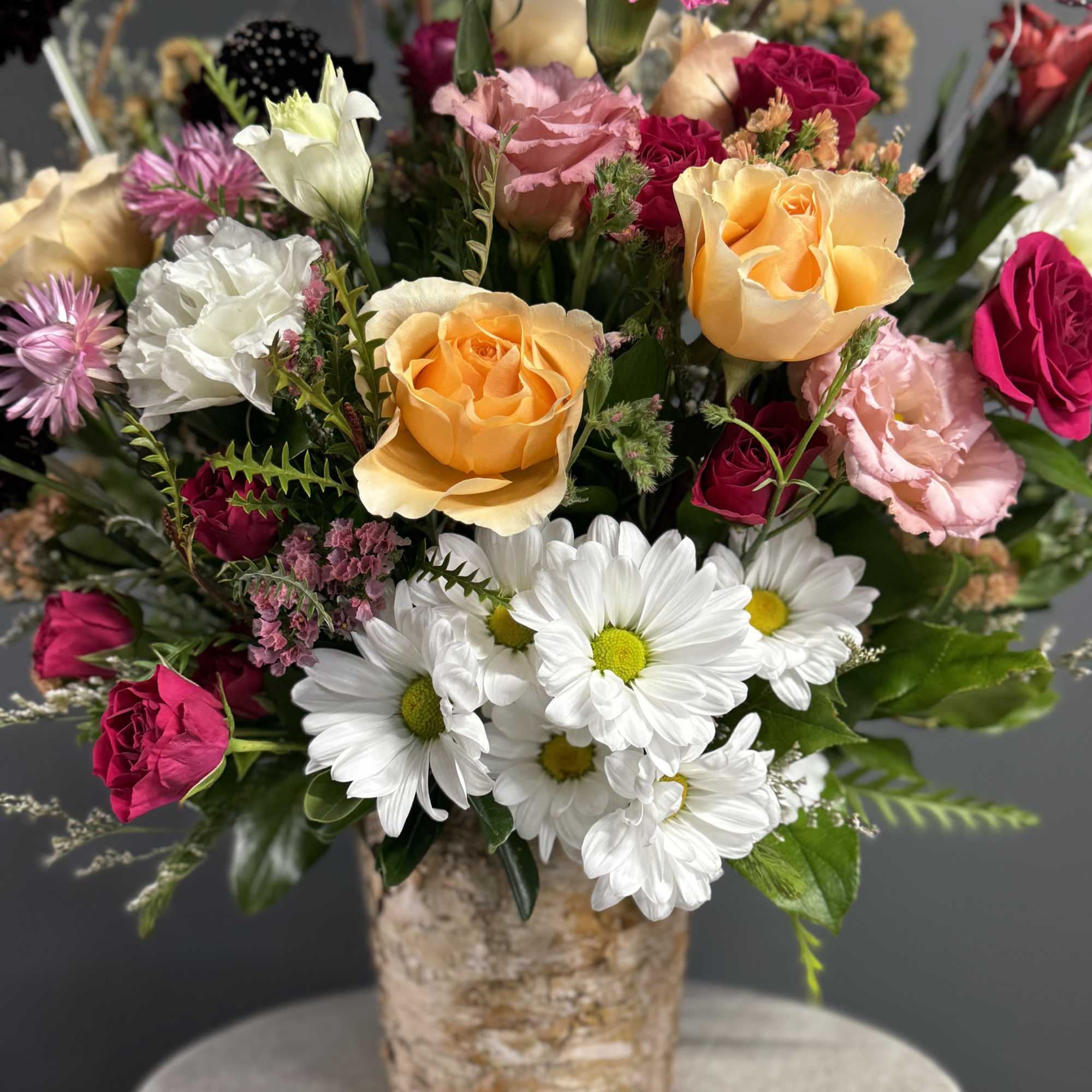 Mixed bouquet of roses and white daisies in a birch-style vase