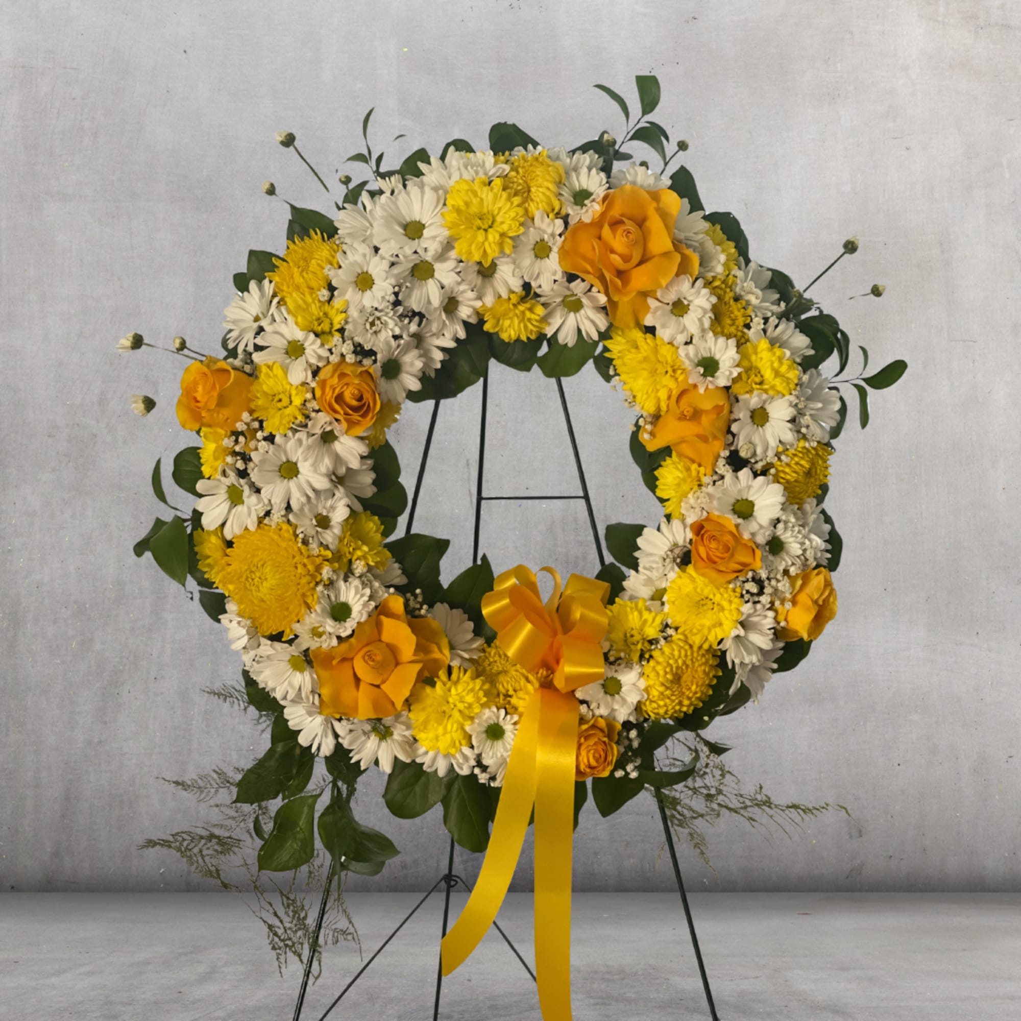 Yellow and white floral wreath on a black stand with a ribbon