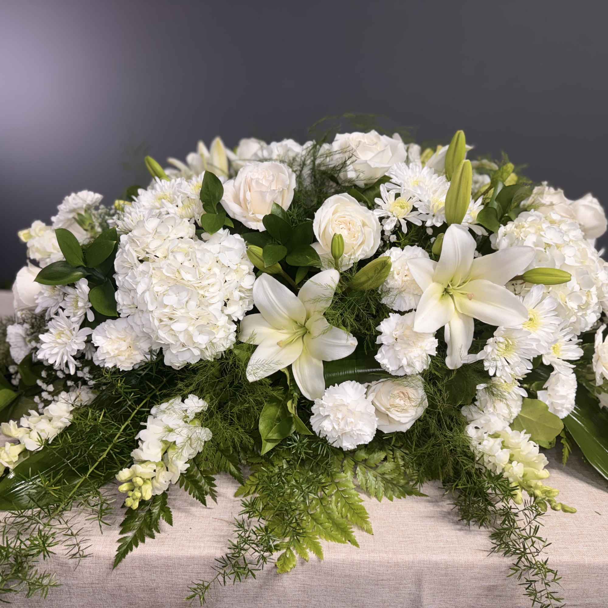 White floral casket spray with lilies, roses, and chrysanthemums