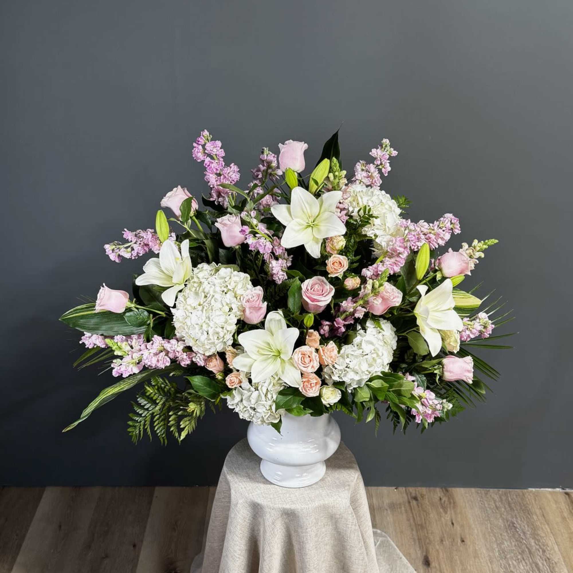 Large pastel floral arrangement in a white vase on a draped pedestal