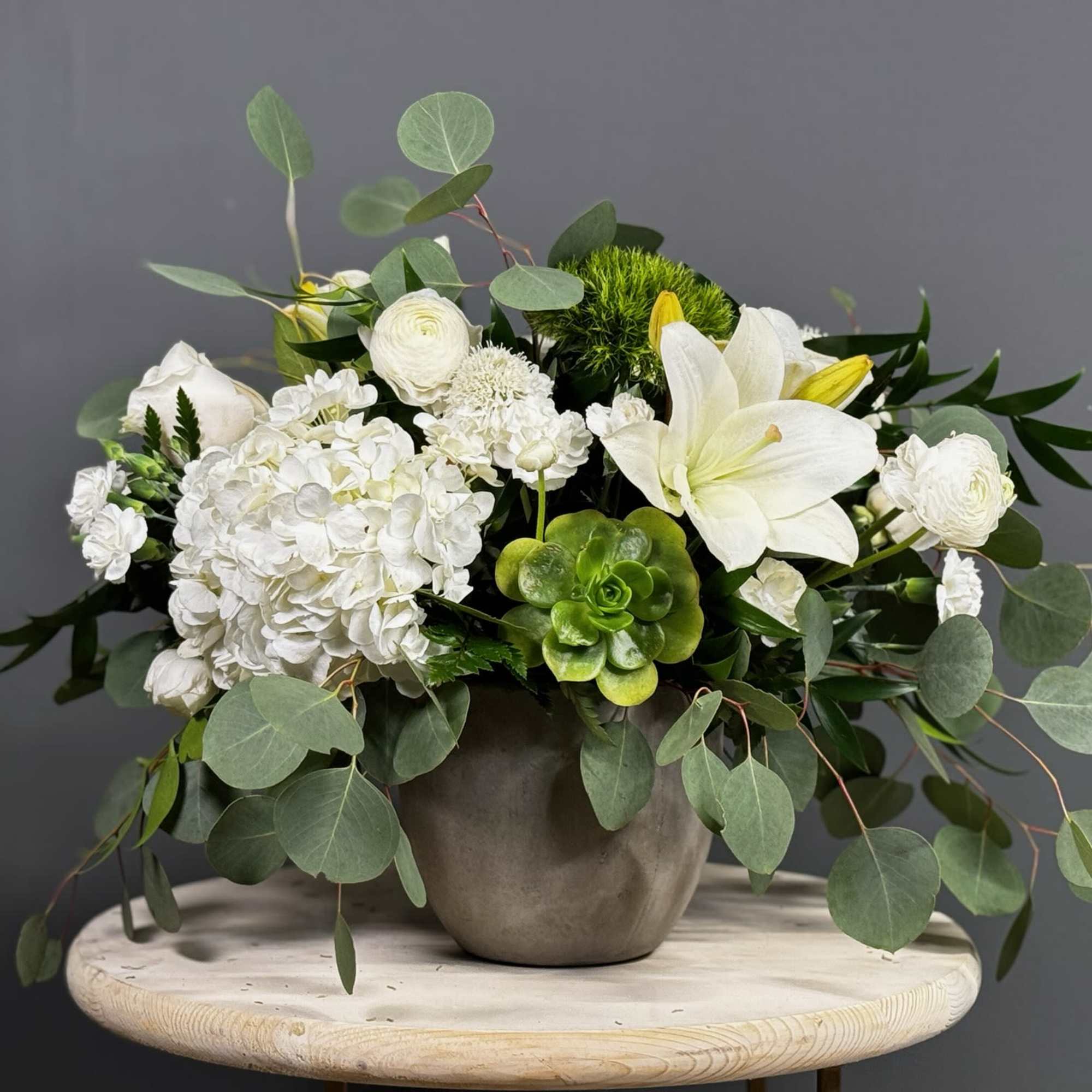 White floral arrangement in a gray vase with eucalyptus and succulents