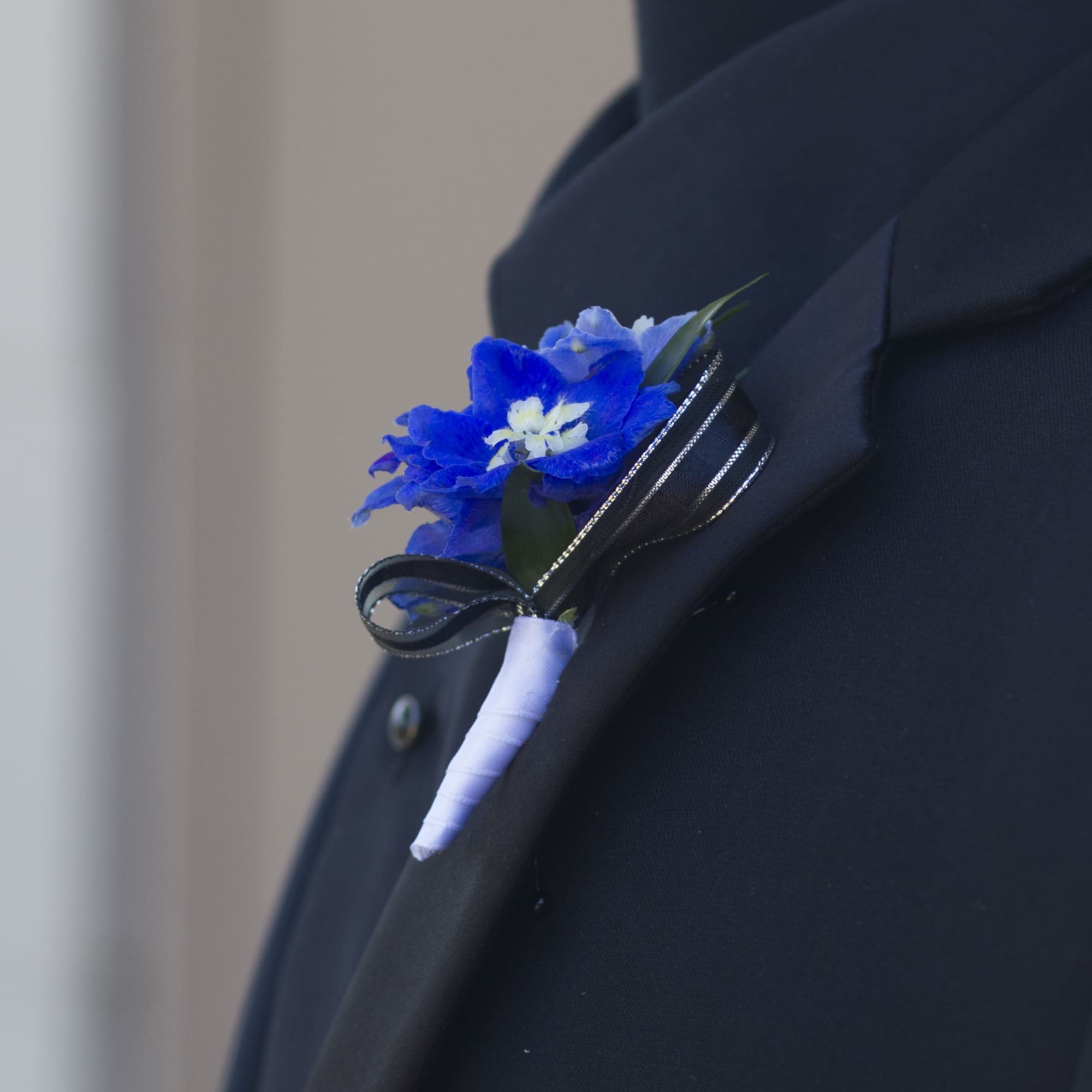 Blue boutonniere with white-wrapped stem and black ribbon bow pinned to a dark suit lapel