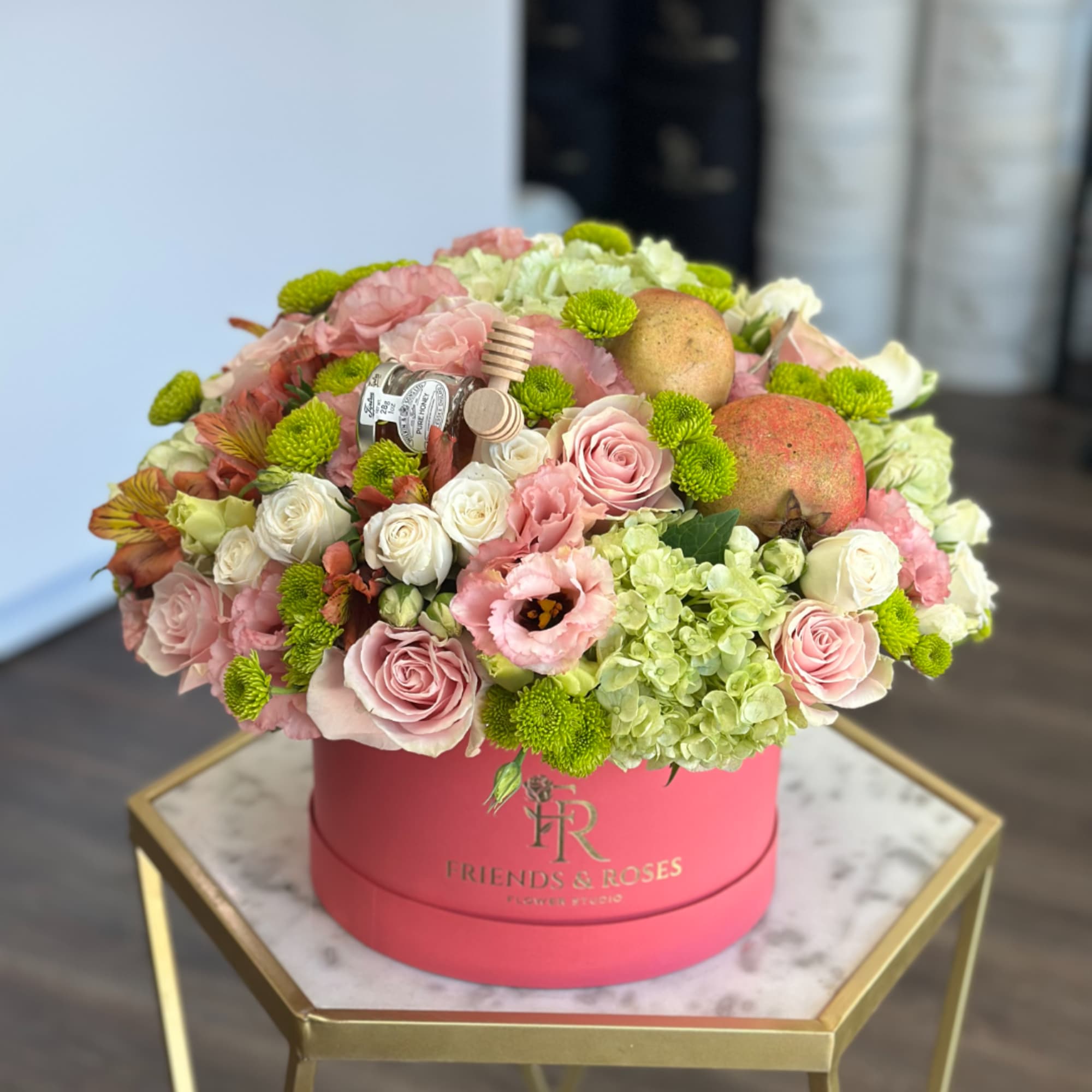 Pink and white roses with green blooms and fruit in a round pink box