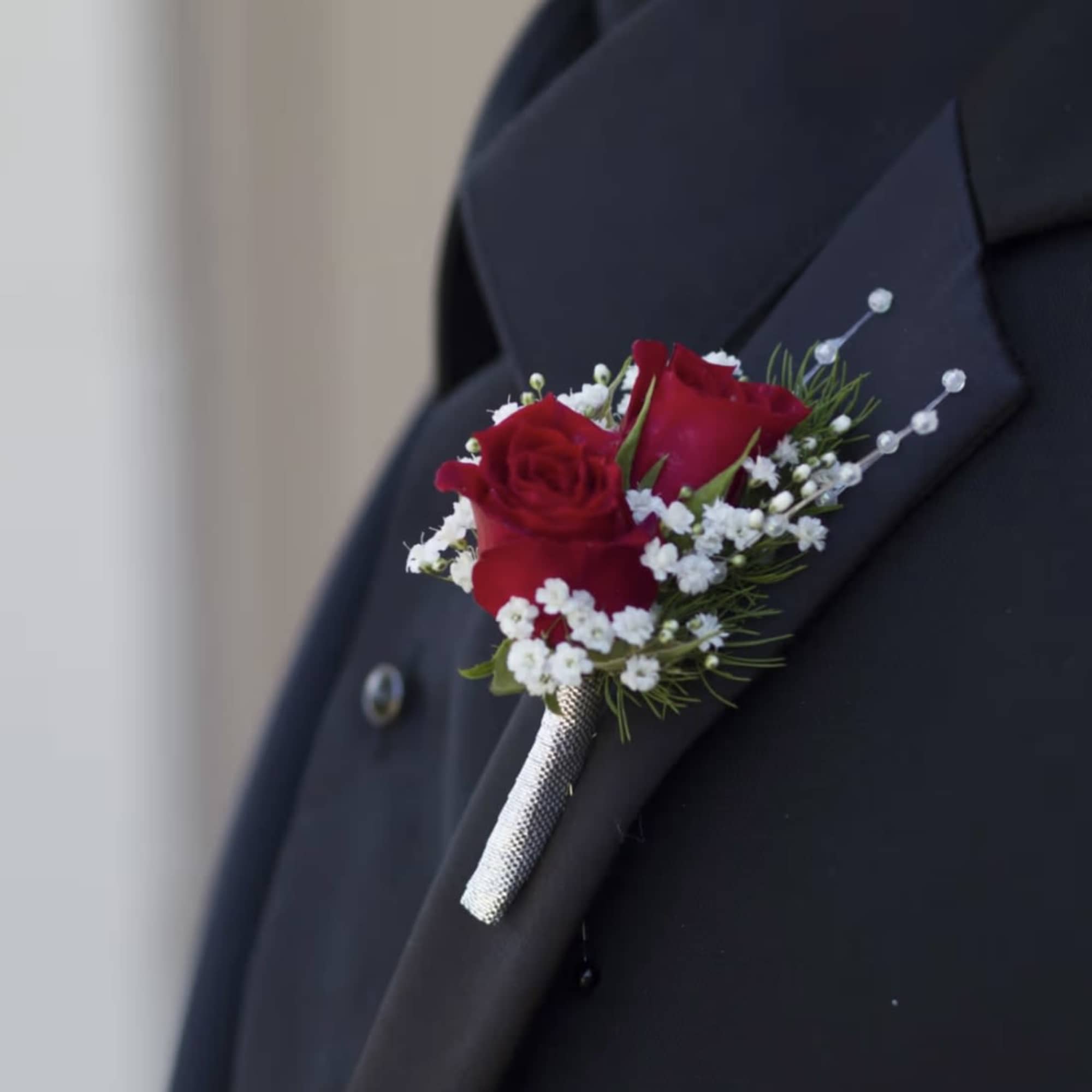 Red rose boutonniere with small white flowers pinned to a black suit lapel