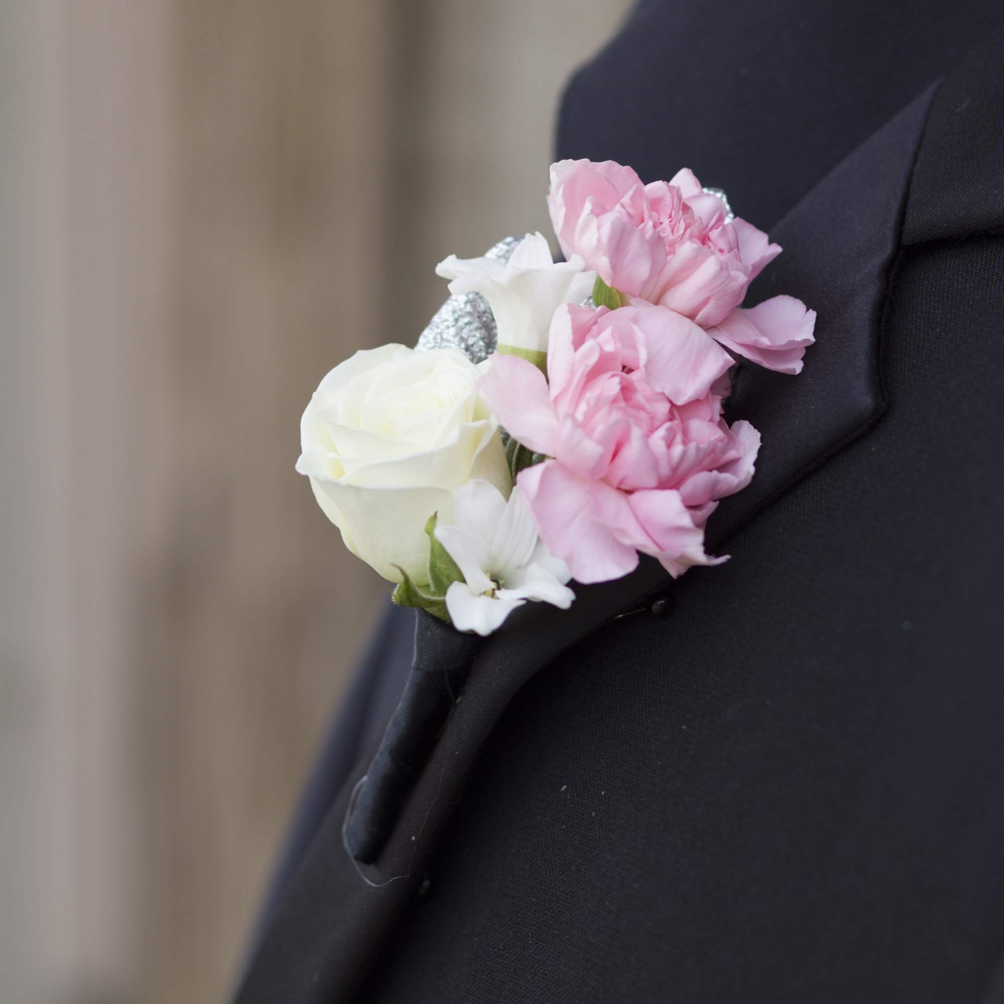 Boutonniere of white rose and pink carnations with rhinestone accents on a black lapel