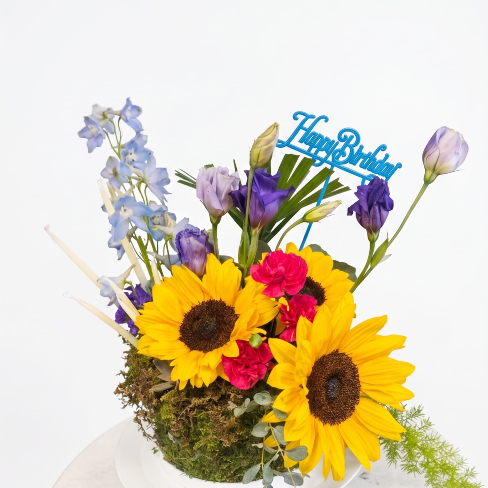 Sunflowers, purple lisianthus, and blue flowers in a moss-covered container with a birthday sign