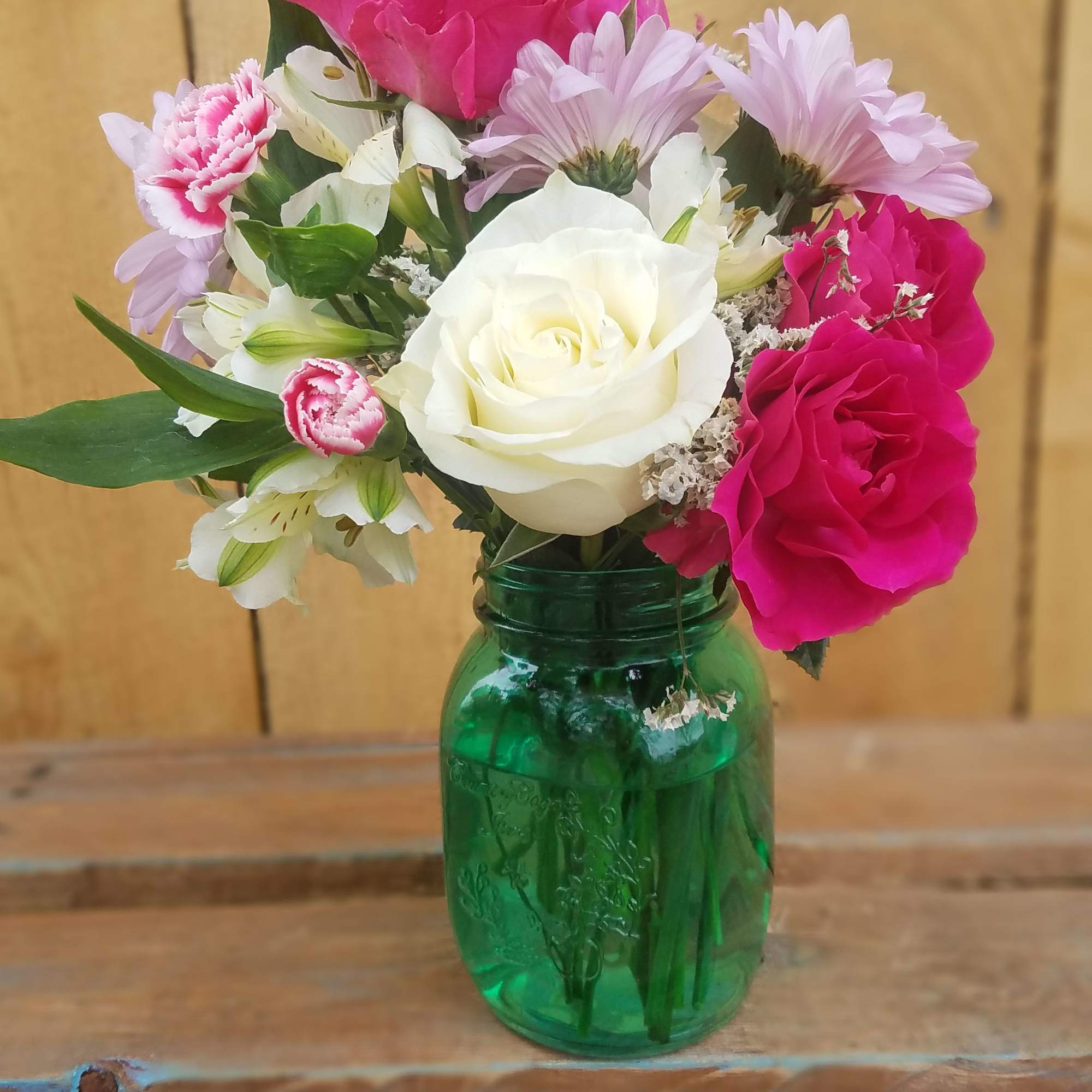 Pink and white flowers arranged in a green glass jar vase