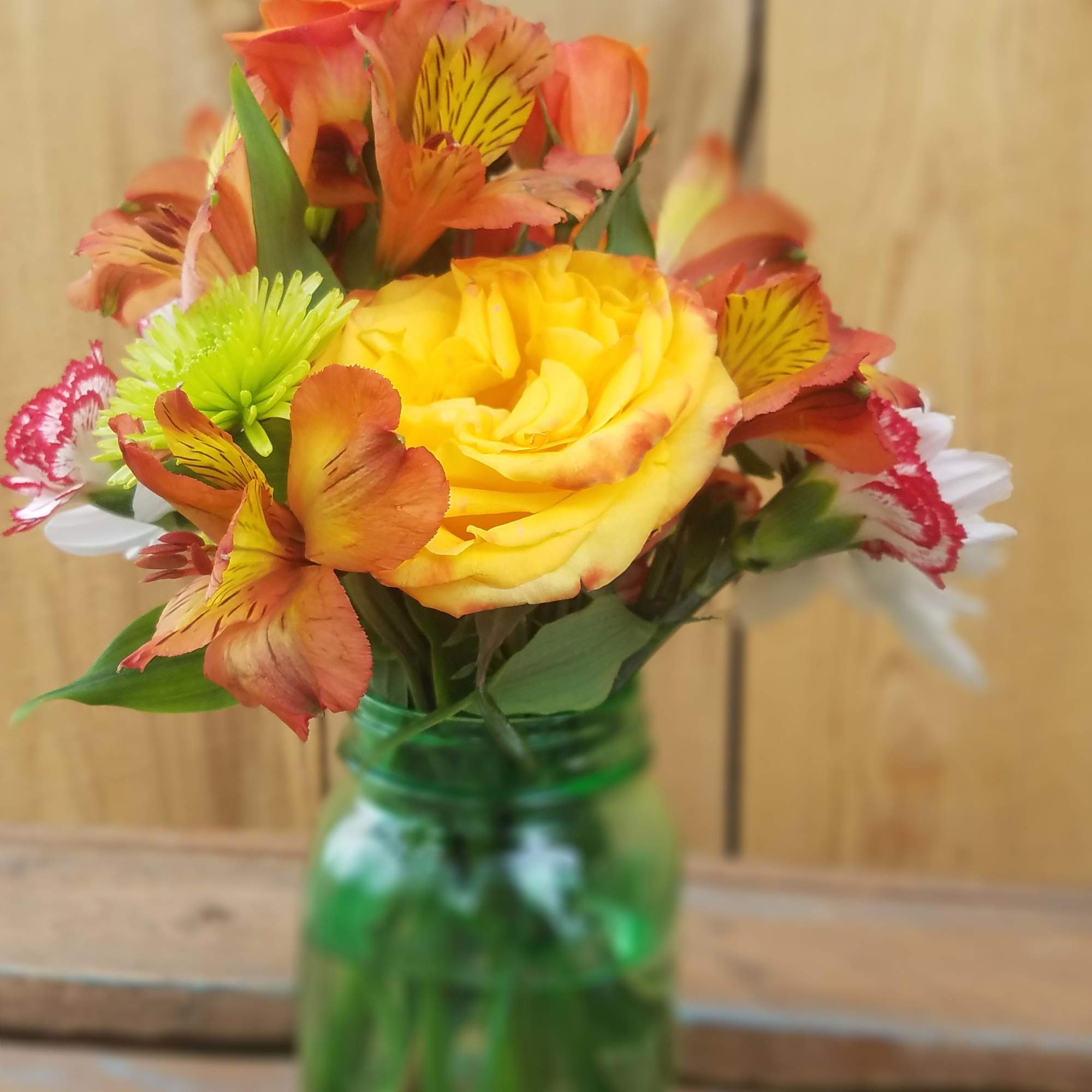 Yellow rose bouquet in a green glass jar with orange and white flowers