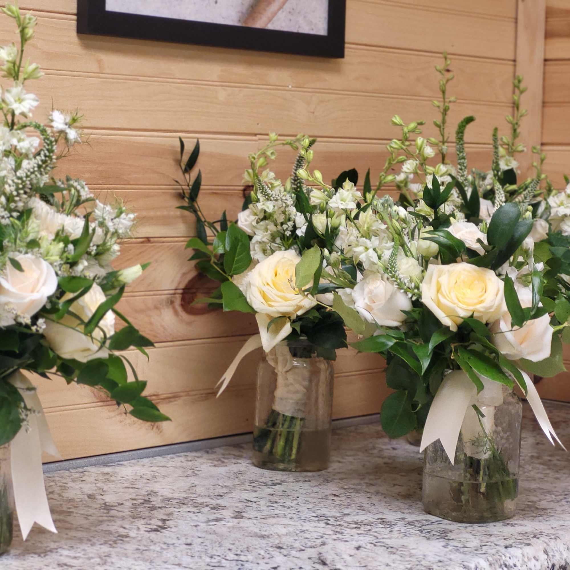 White rose bouquets in glass jars with greenery and ribbon