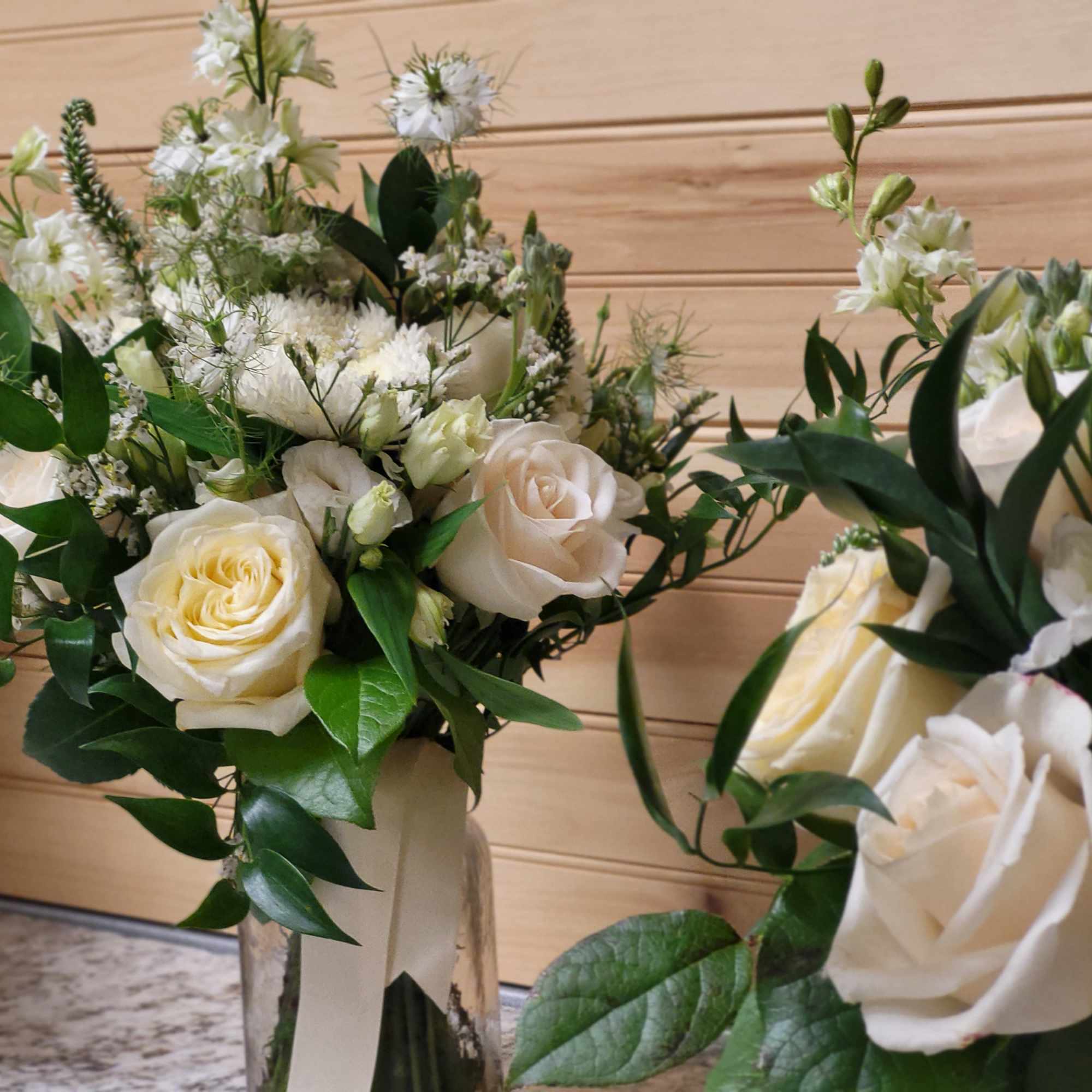 White rose bouquets with greenery in clear glass vases