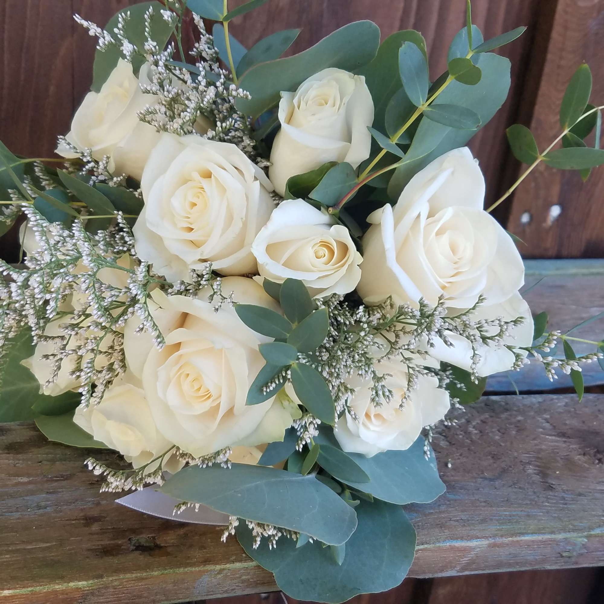 Hand-tied bouquet of cream roses with white filler flowers and eucalyptus, resting on rustic wooden boards.