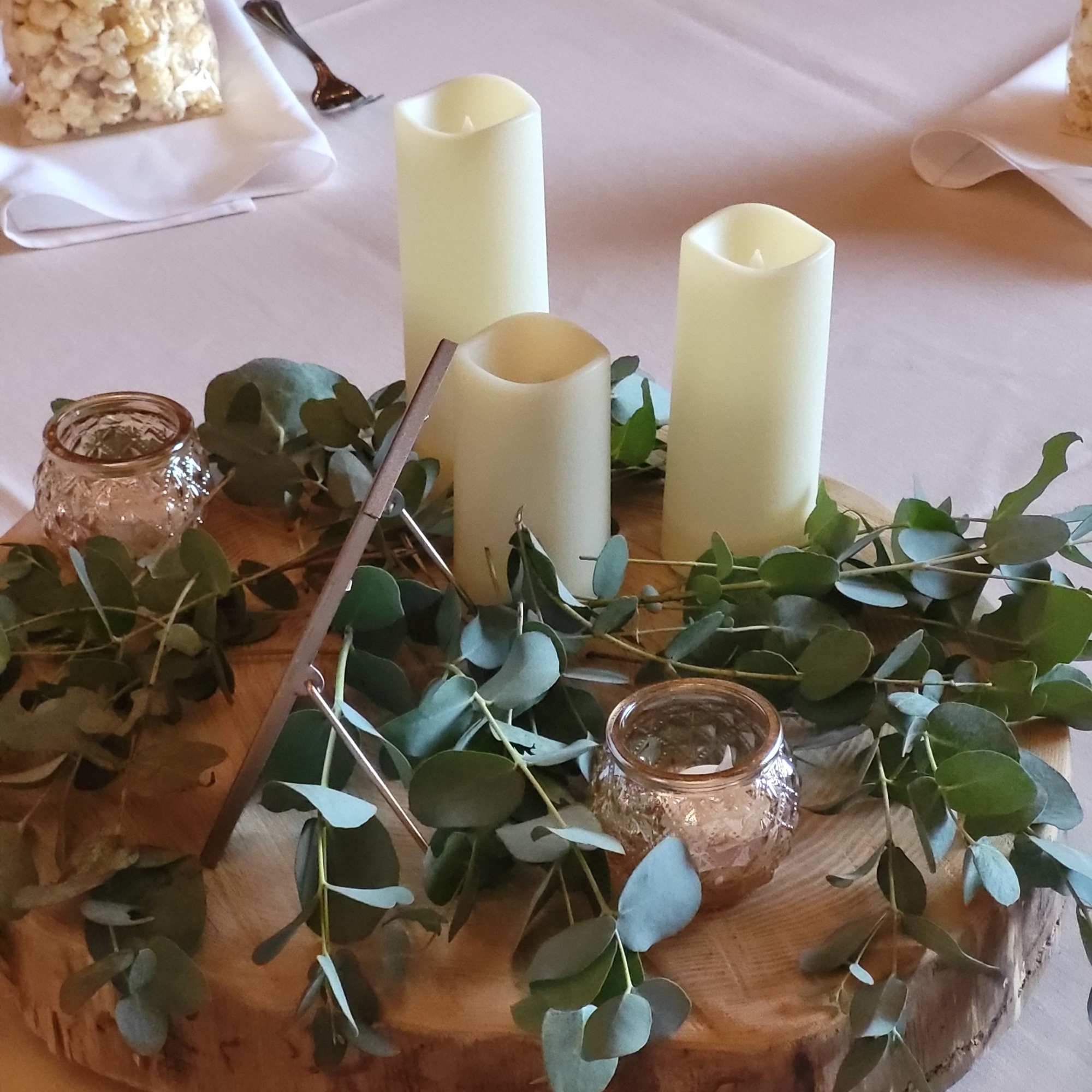 Eucalyptus garland around three ivory pillar candles on a wood slice centerpiece