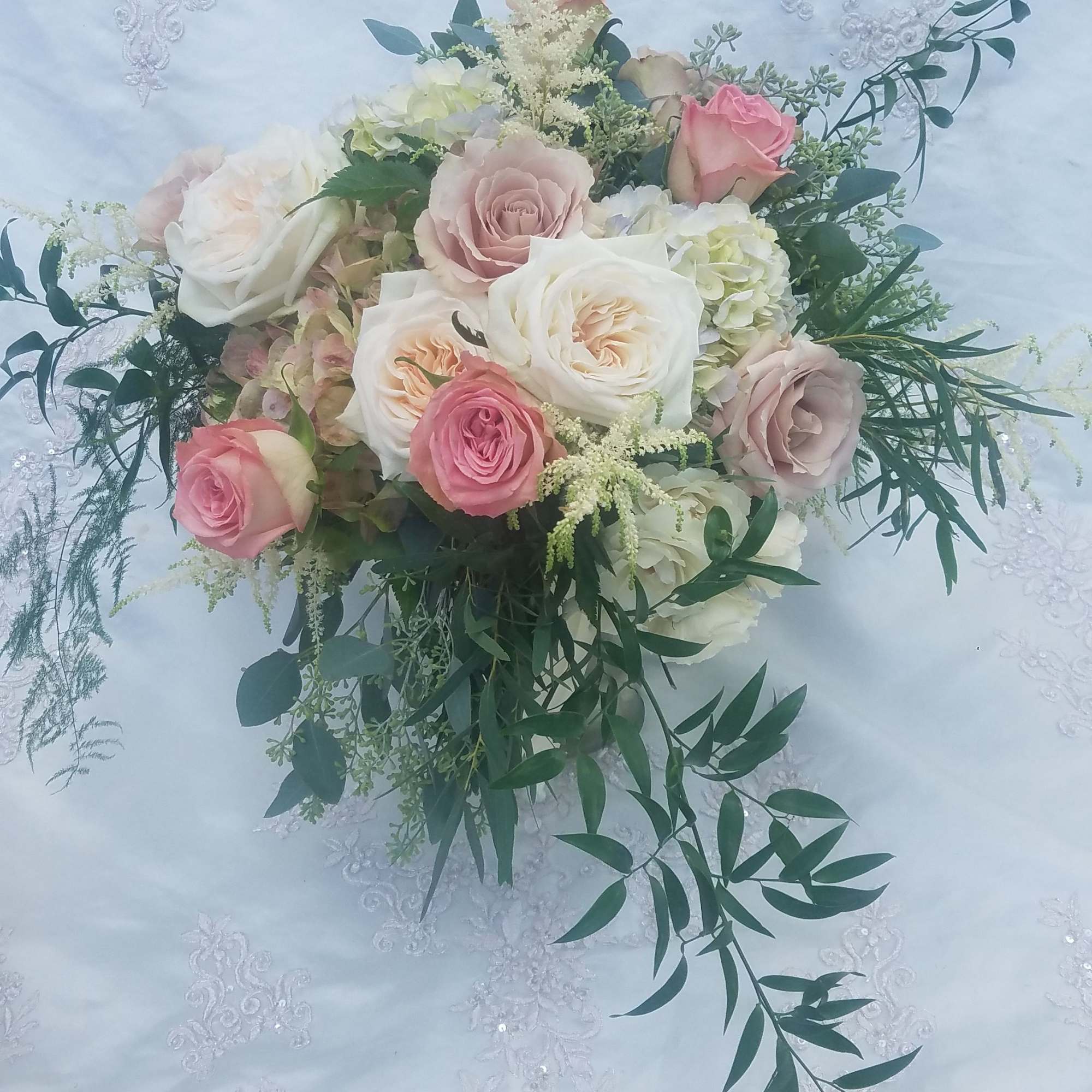 Pastel rose bouquet with white and pink blooms on embroidered fabric