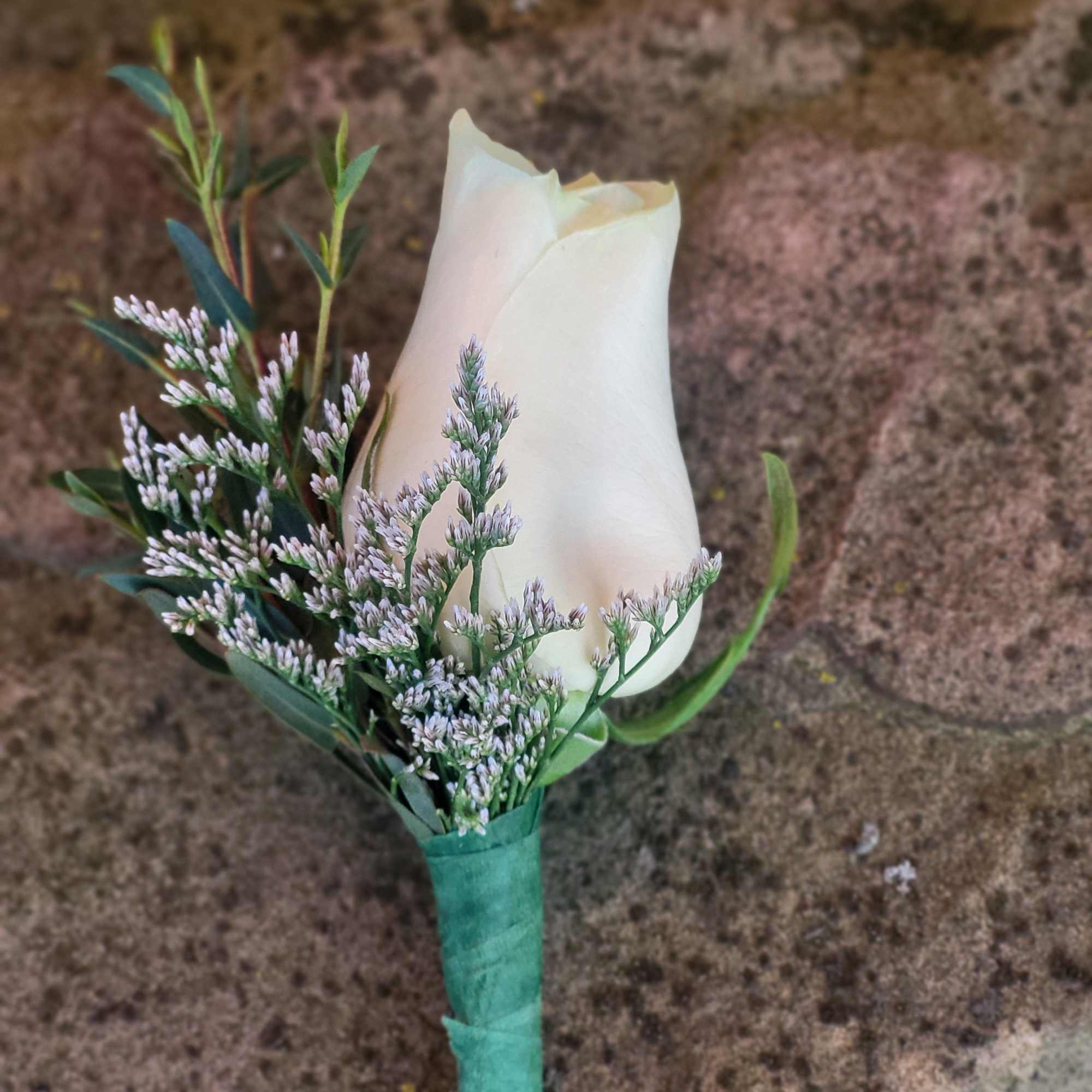 White rose boutonniere with tiny lavender filler flowers wrapped in green floral tape