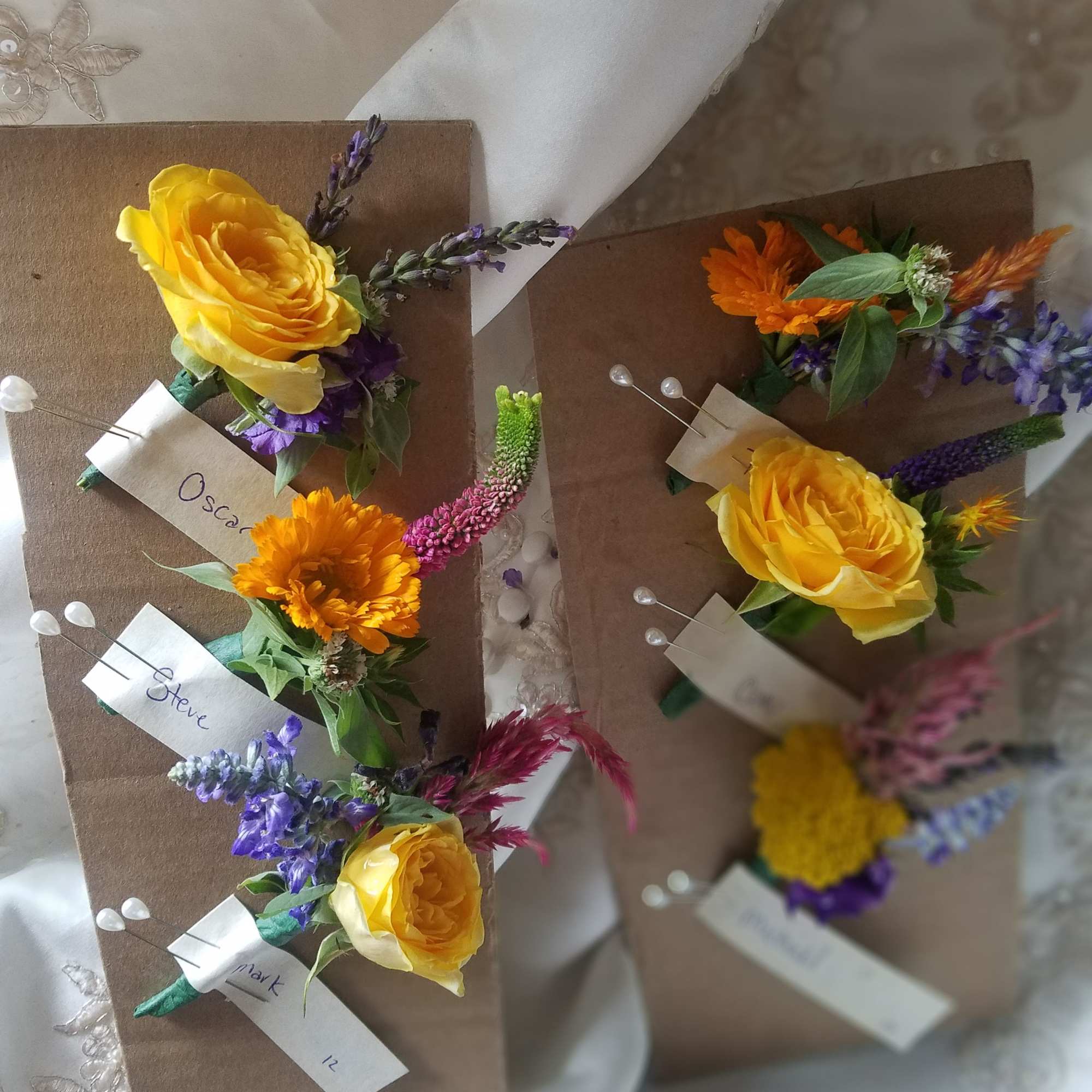 Small floral boutonnieres with yellow roses and purple accents on brown cards