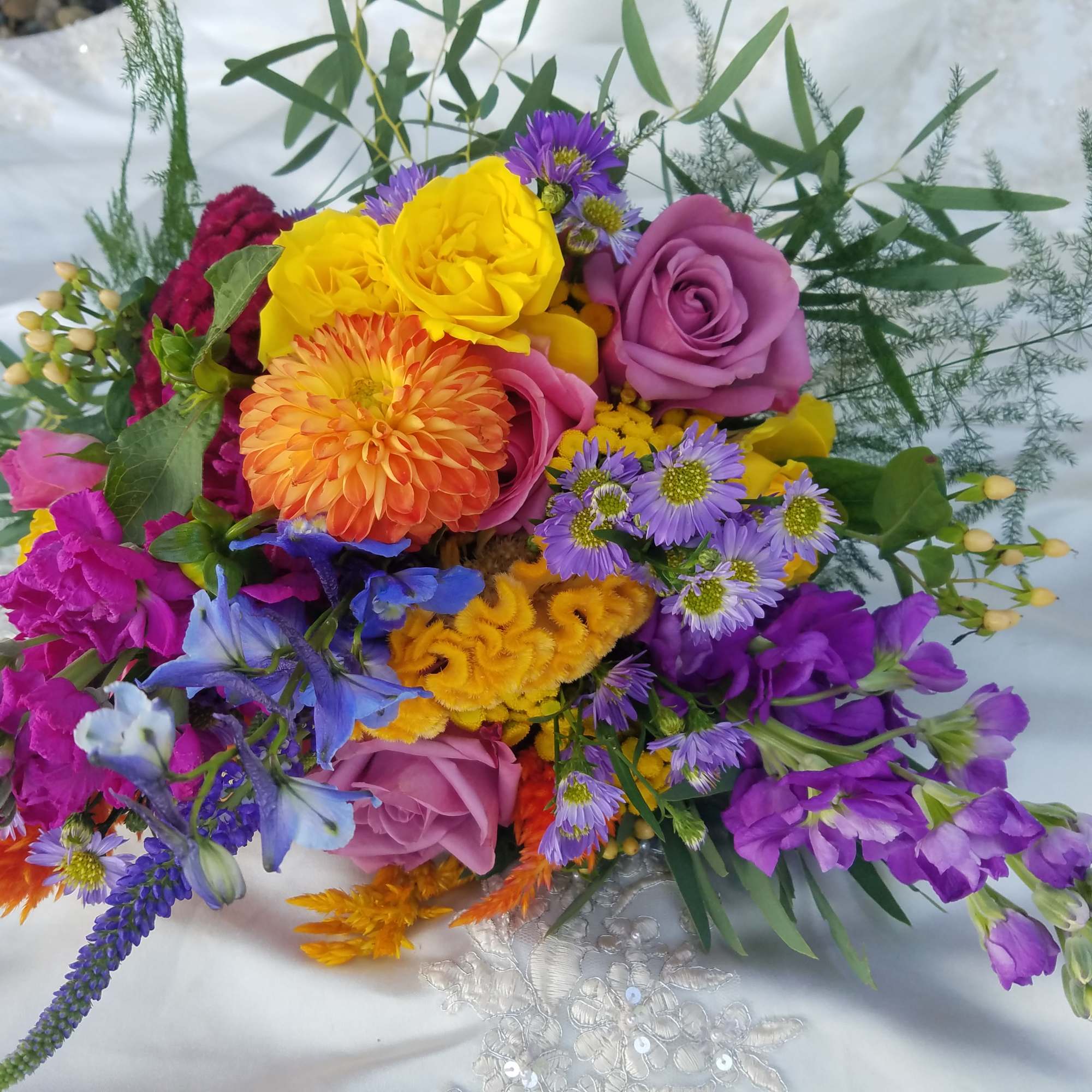Colorful bouquet with roses, dahlias, and purple flowers on white fabric