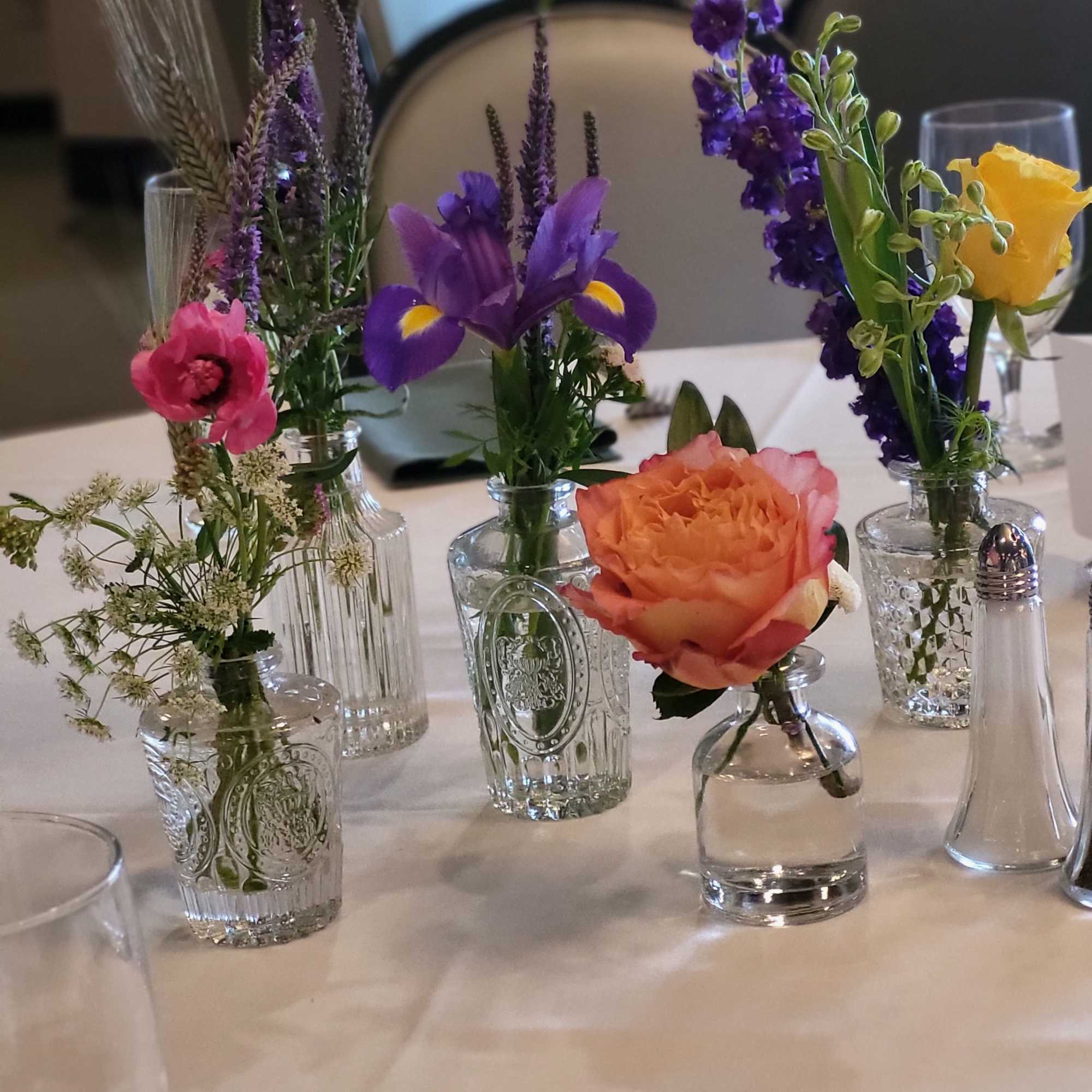Small mixed flower arrangements in clear glass vases on a table, photo 5 of 8