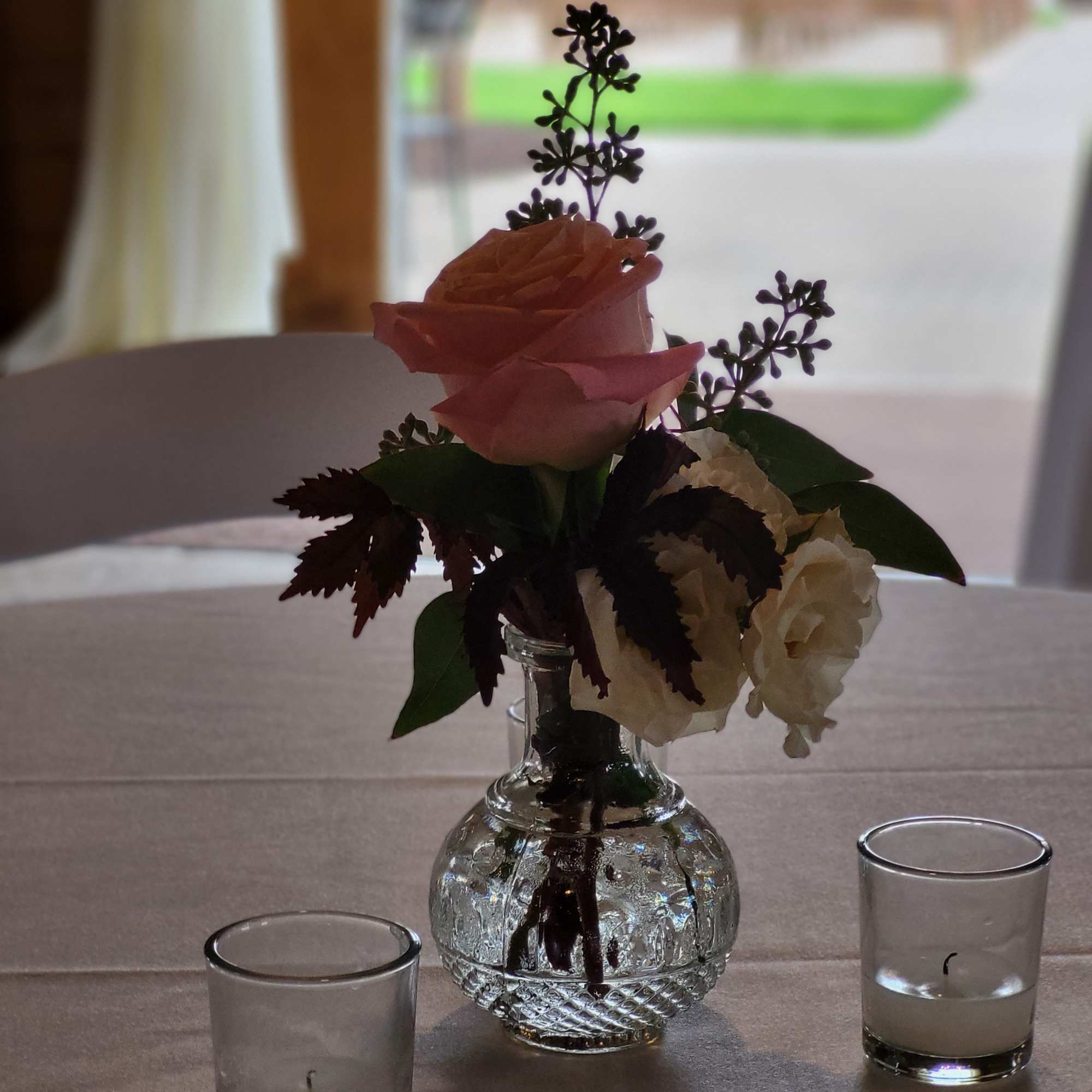 Pink and white roses in a small glass vase with two votive candles