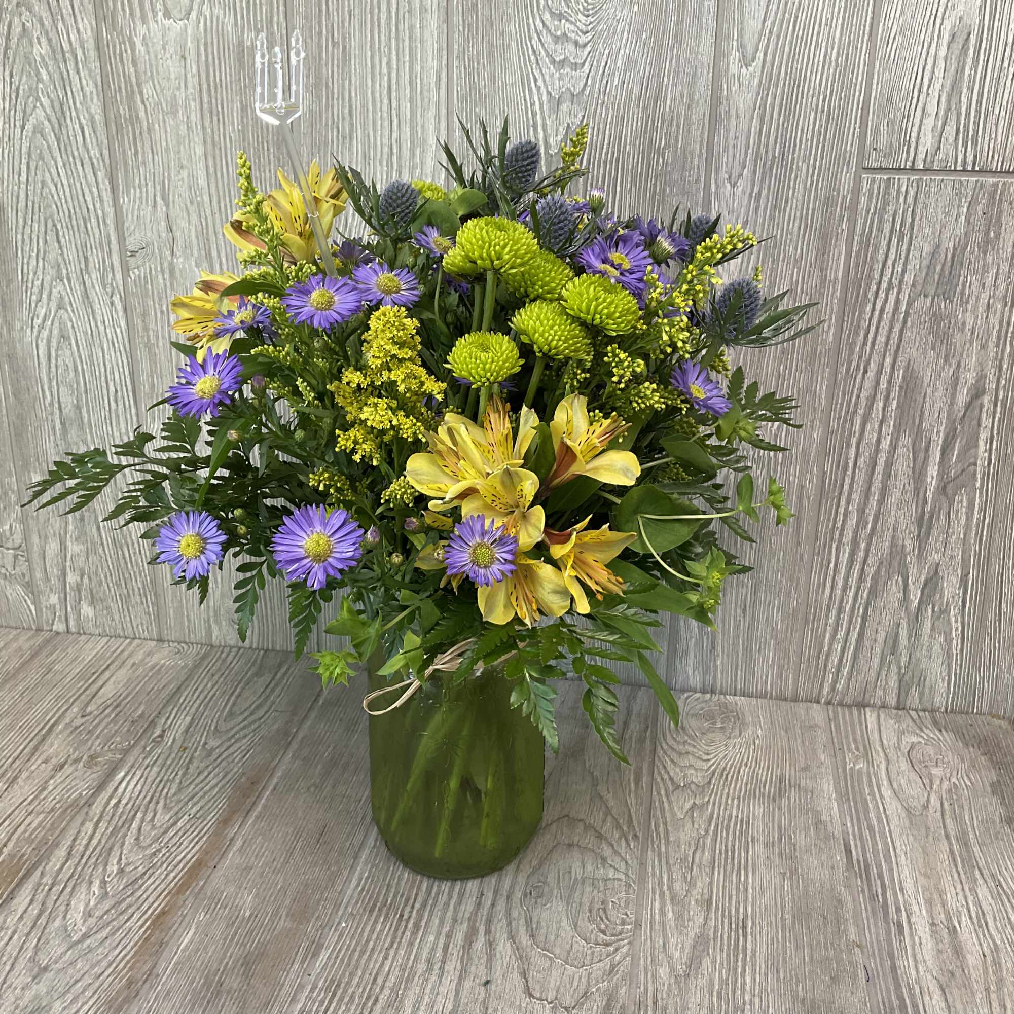 Bouquet of yellow and purple flowers in a green glass vase