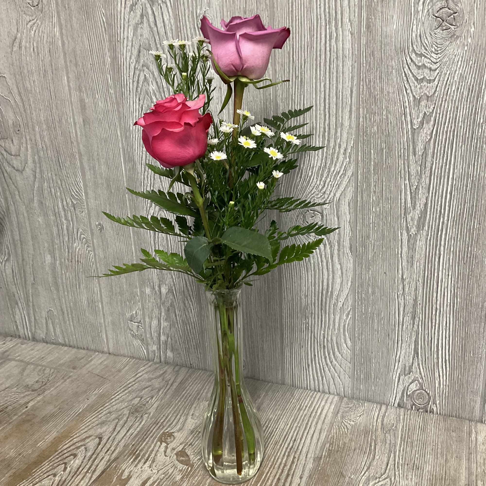 Two pink roses in a clear glass vase with small white filler flowers