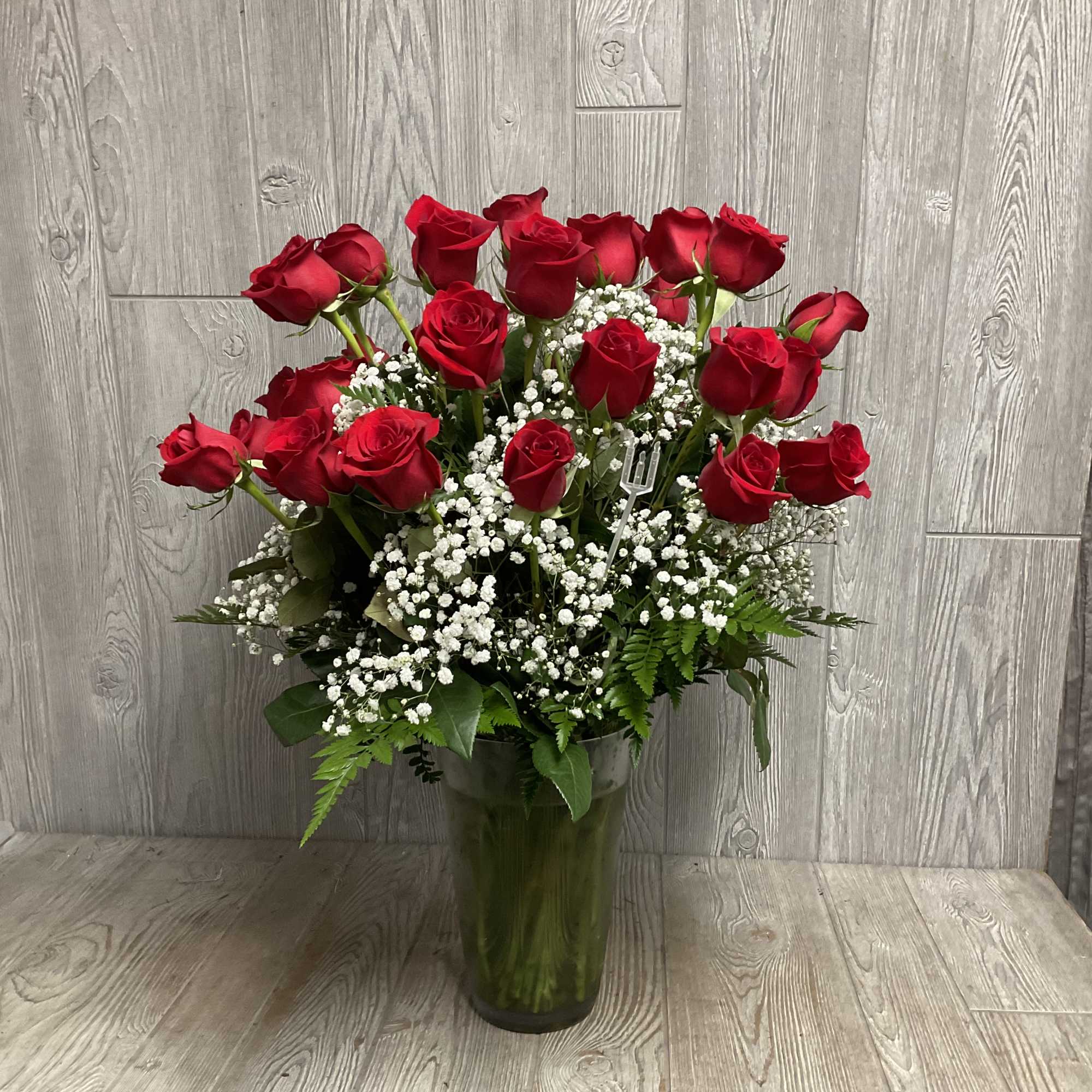 Red roses arranged in a tall glass vase with white baby's breath
