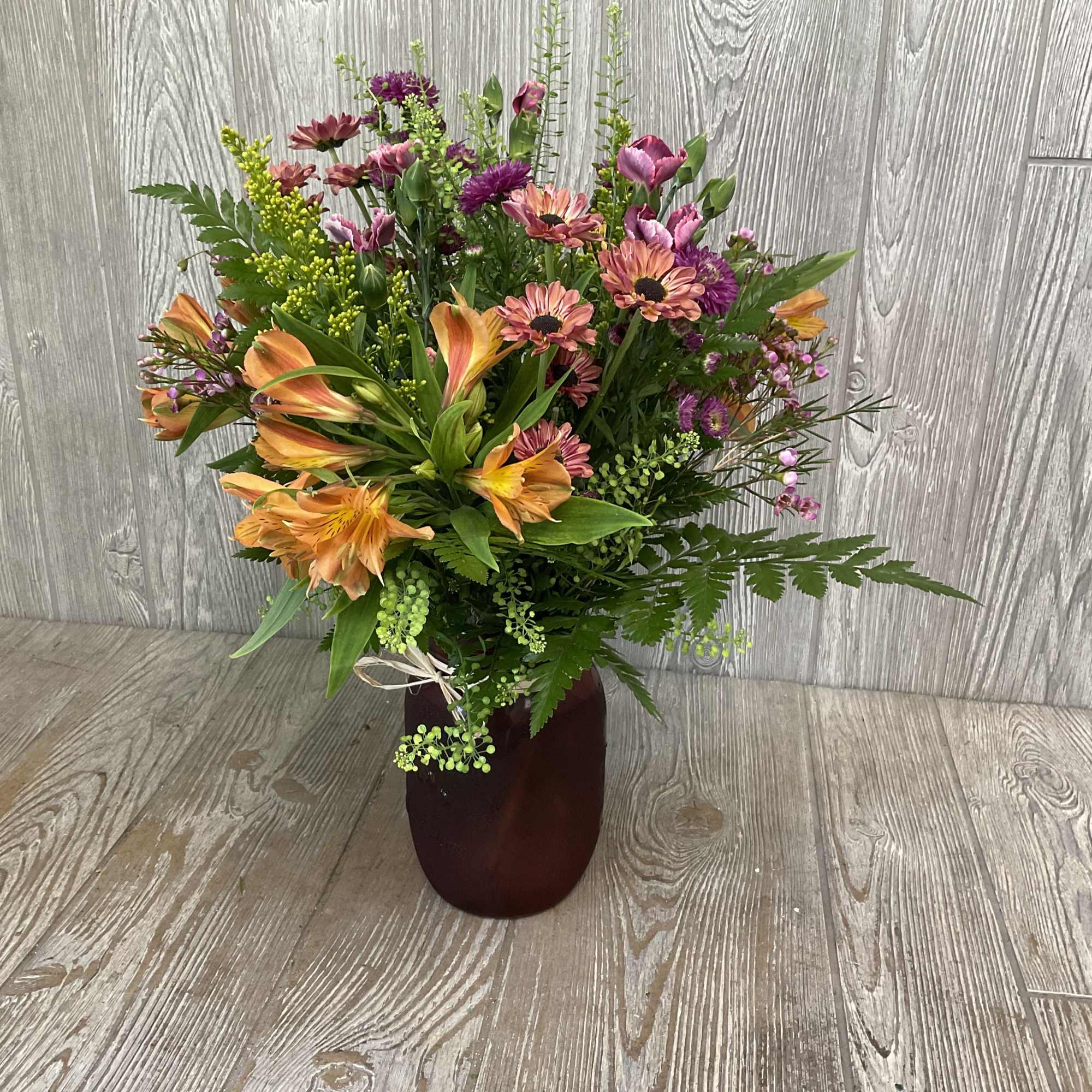 Mixed bouquet of orange lilies and pink-purple daisies in a dark vase