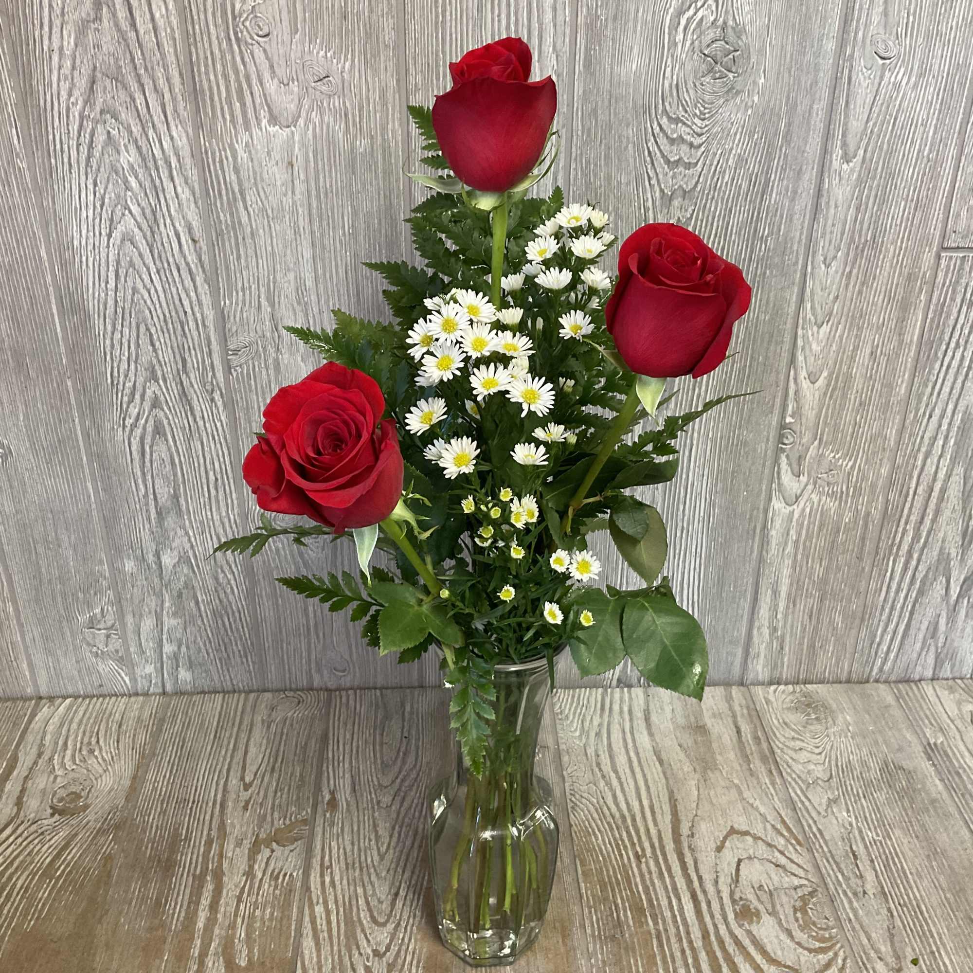 Three red roses with white daisies in a clear glass vase