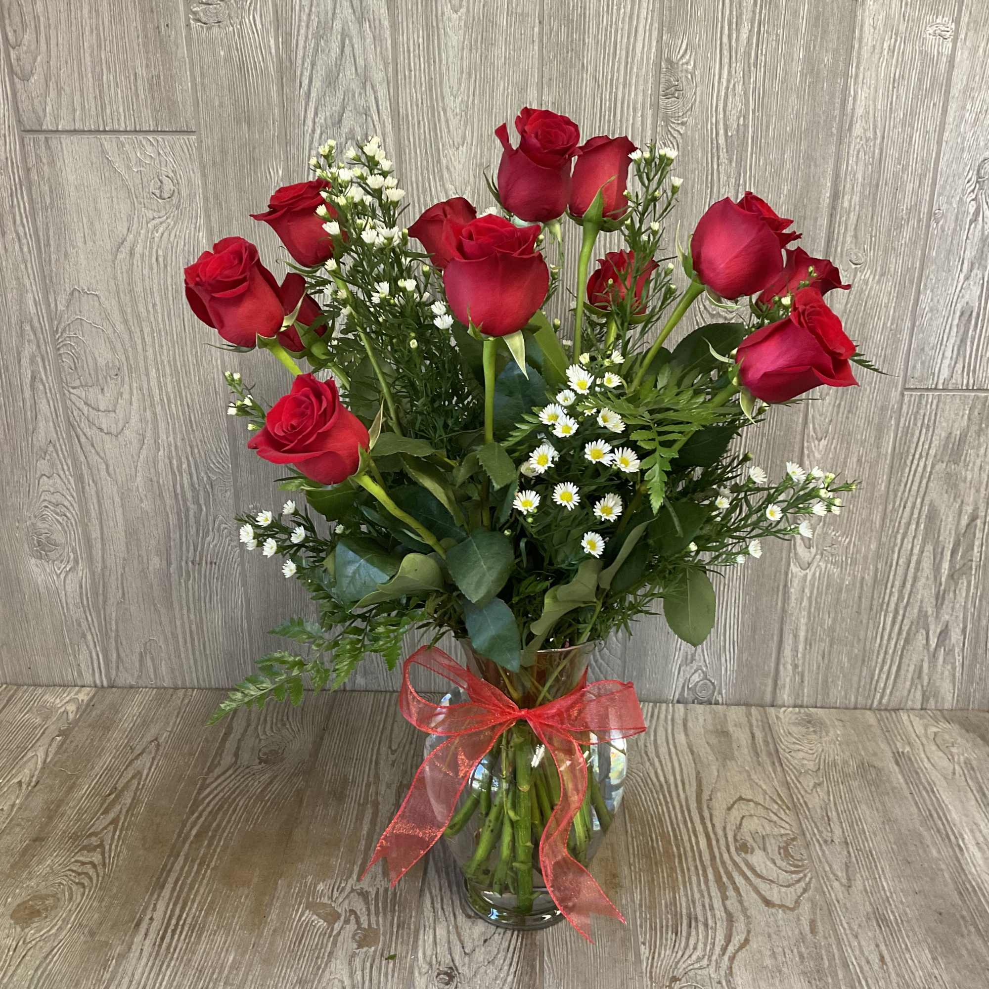 Bouquet of red roses and small white filler flowers in a glass vase with a red ribbon