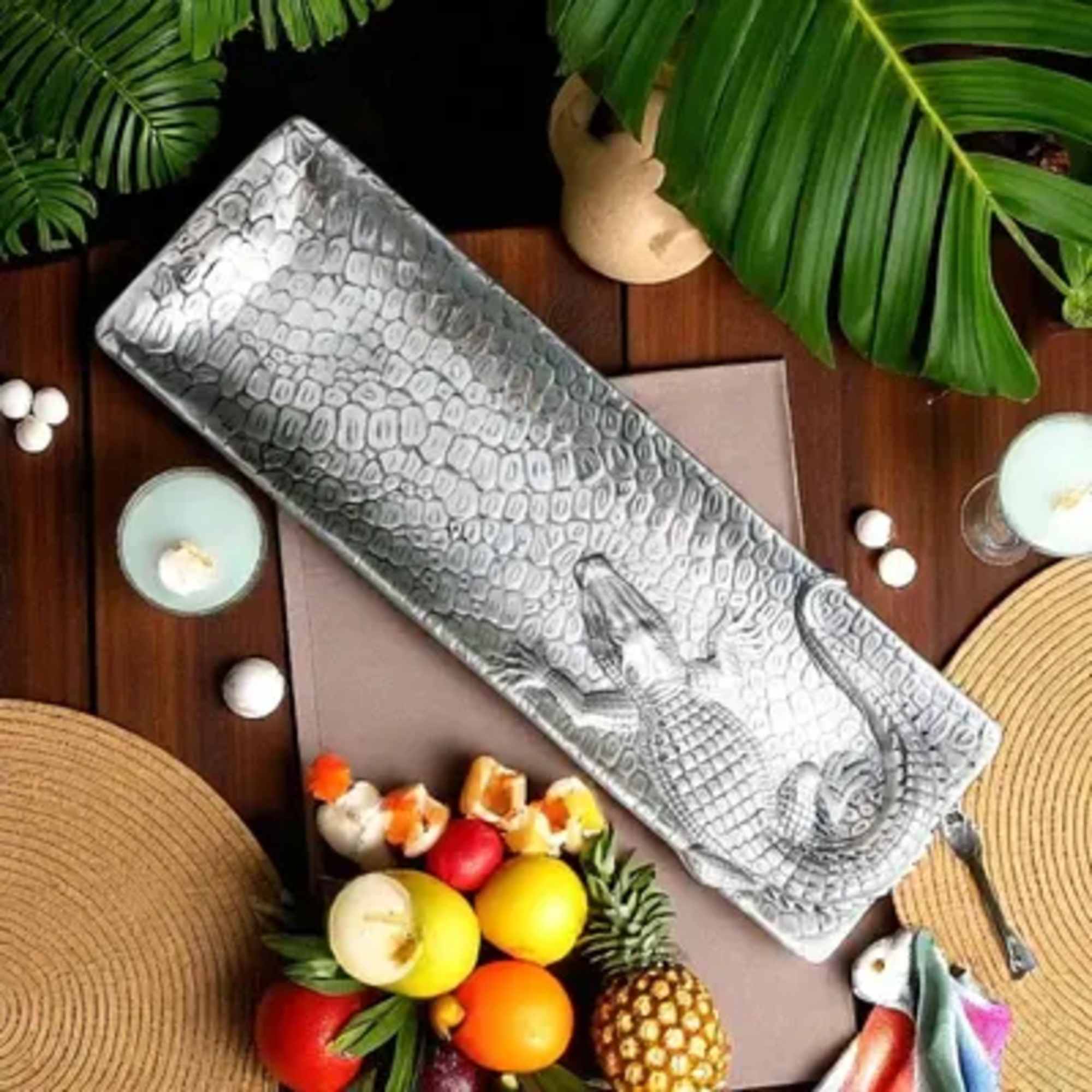 Silver crocodile-texture clutch on a table with candles and fruit