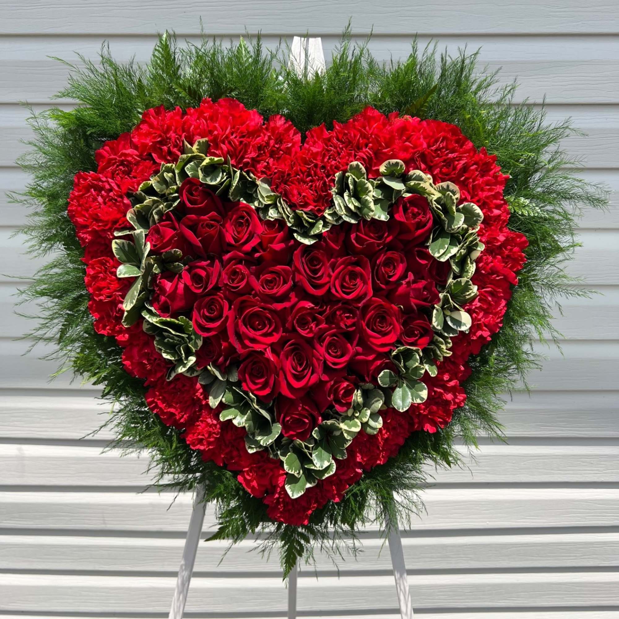 Heart-shaped red rose and carnation standing spray on an easel