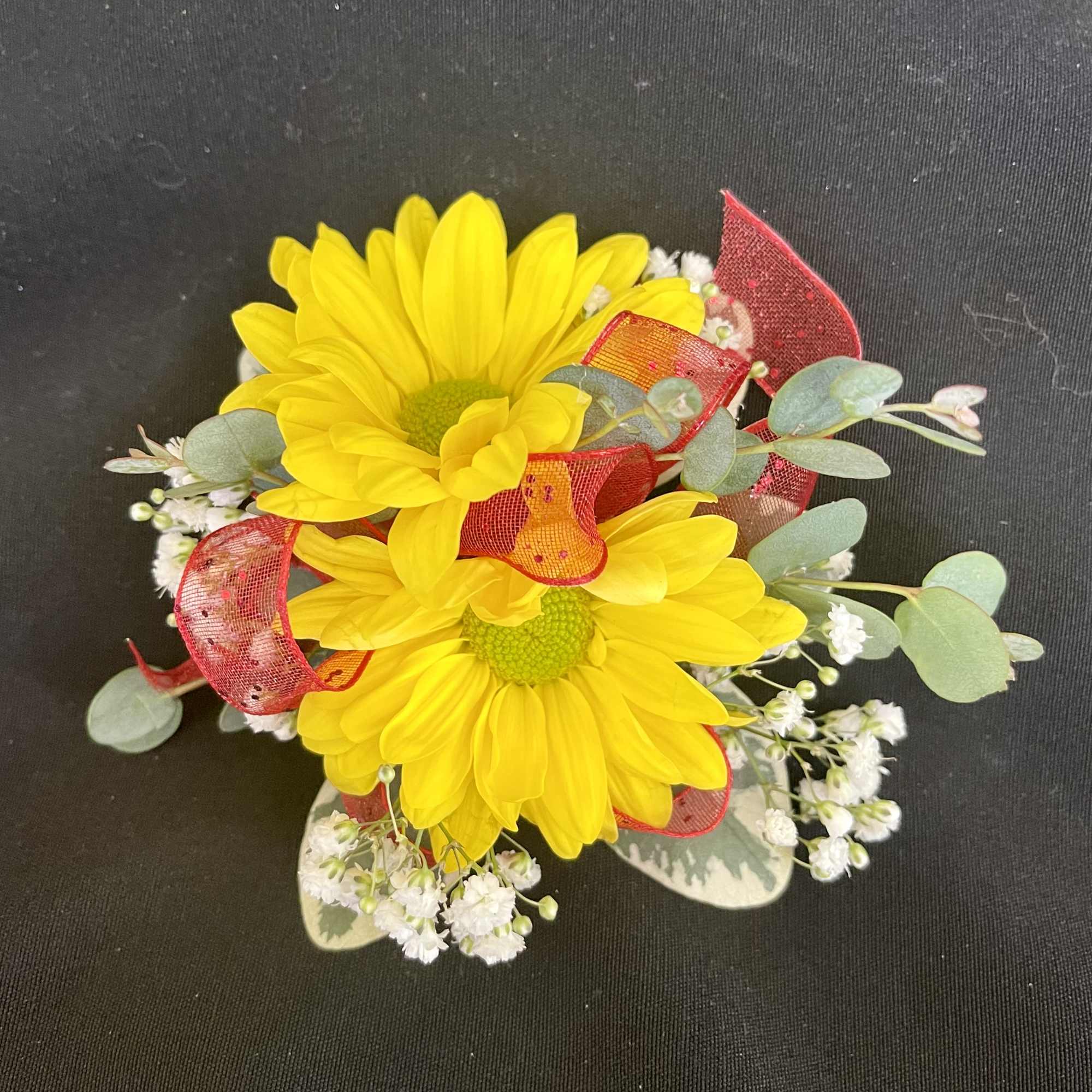 Yellow daisy bouquet with red ribbon accents on a dark background