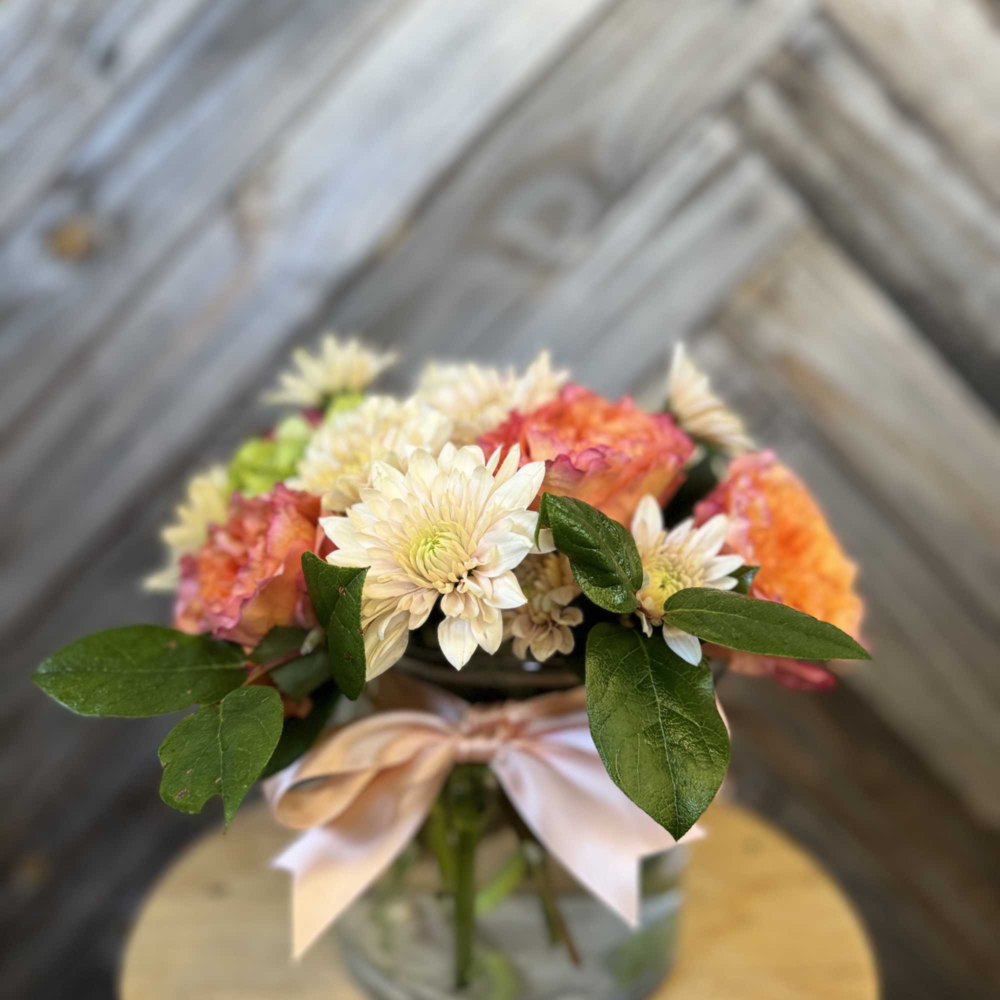 Bouquet of peach and white flowers in a glass vase with a ribbon