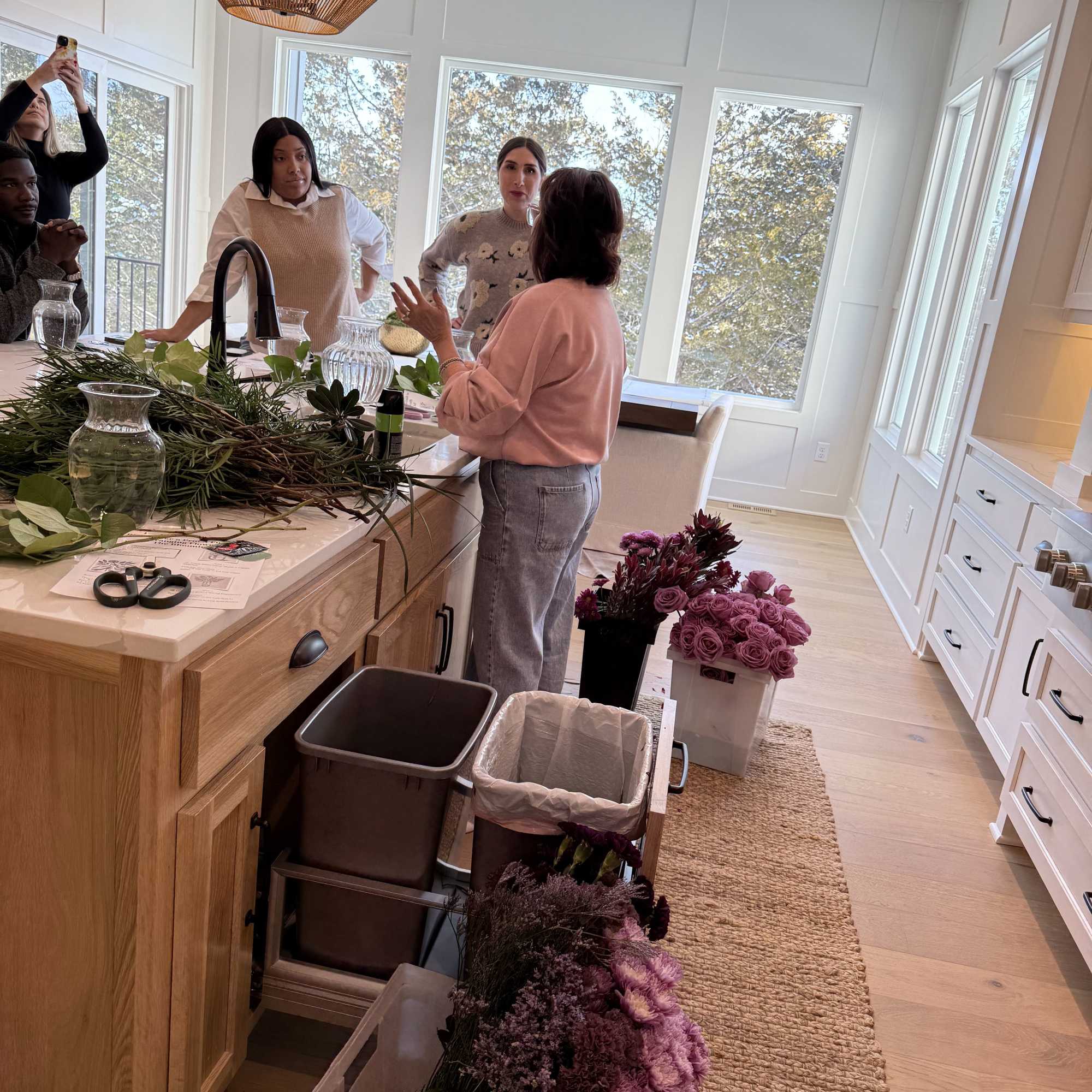 People arranging purple flowers and greenery on a kitchen island