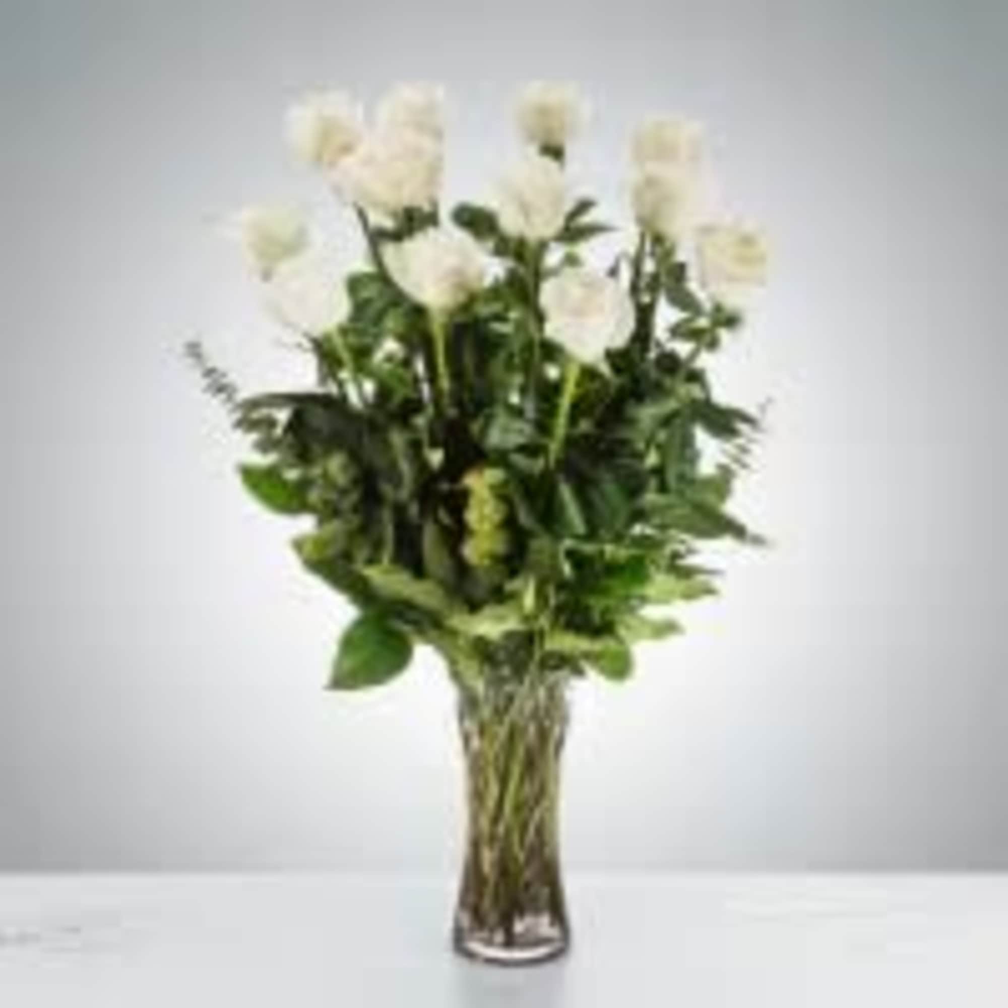 White roses in a tall glass vase with greenery