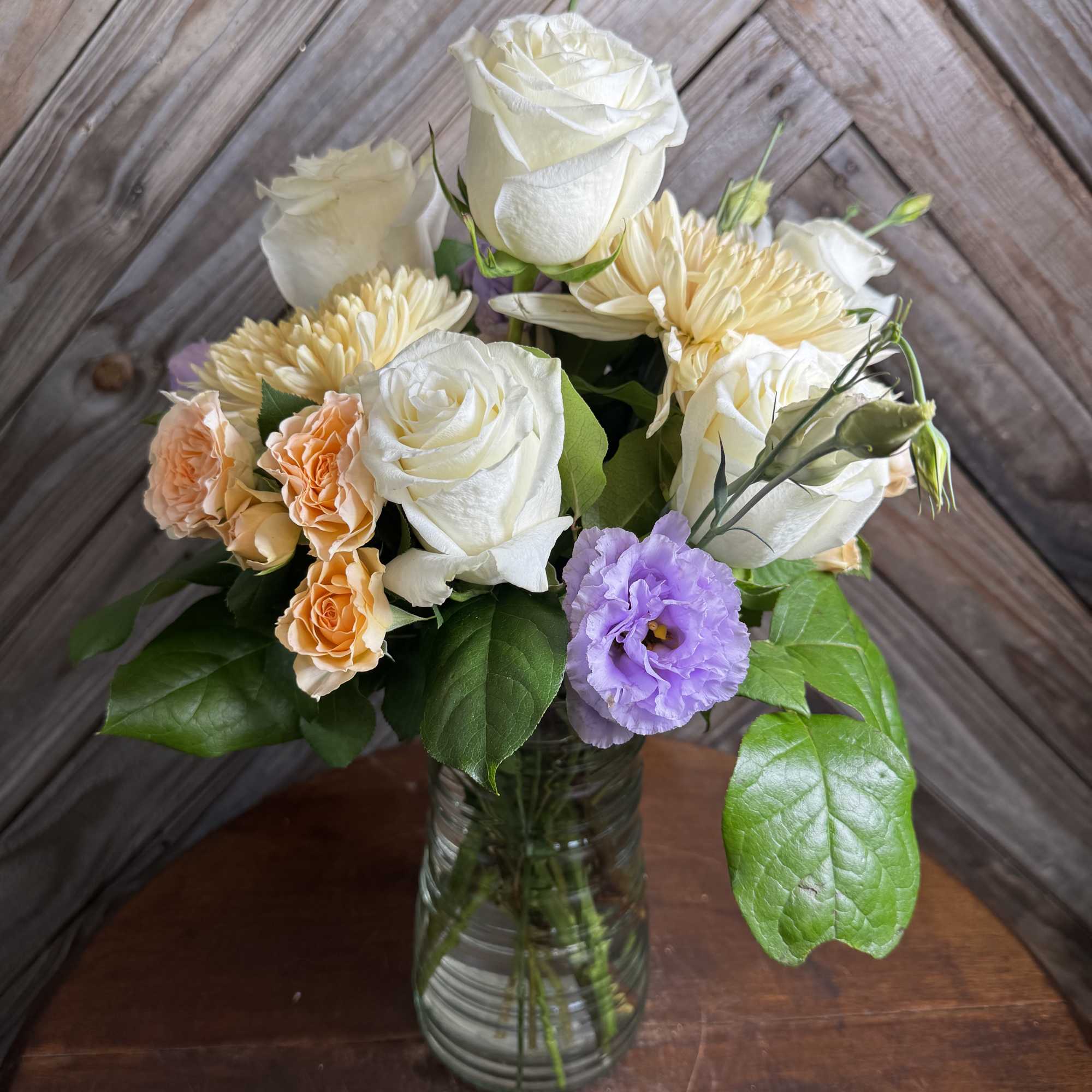 Bouquet of white roses, peach spray roses, and lavender blooms in a glass vase.