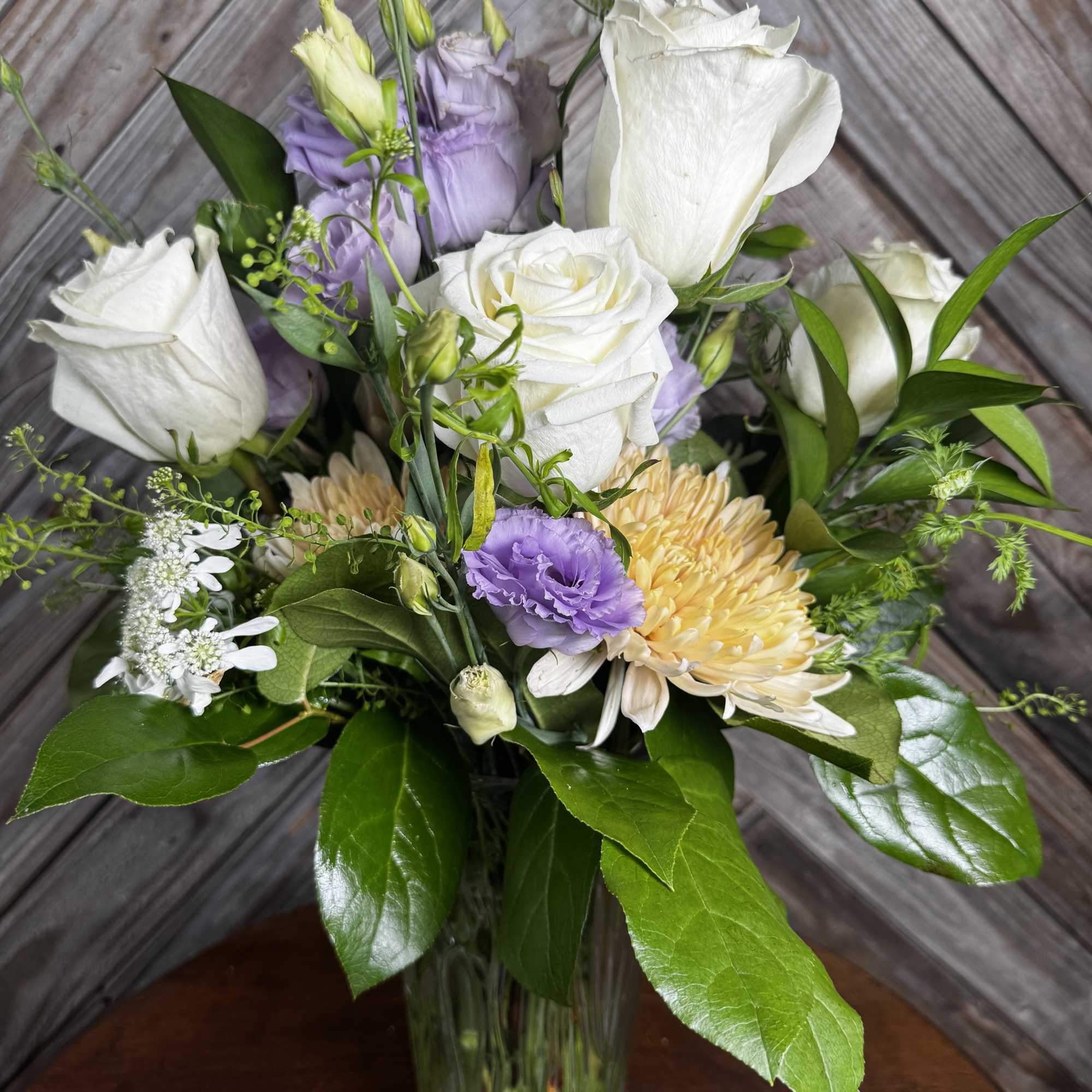 Bouquet of white roses, lavender blooms, and pale yellow flowers in a glass vase.