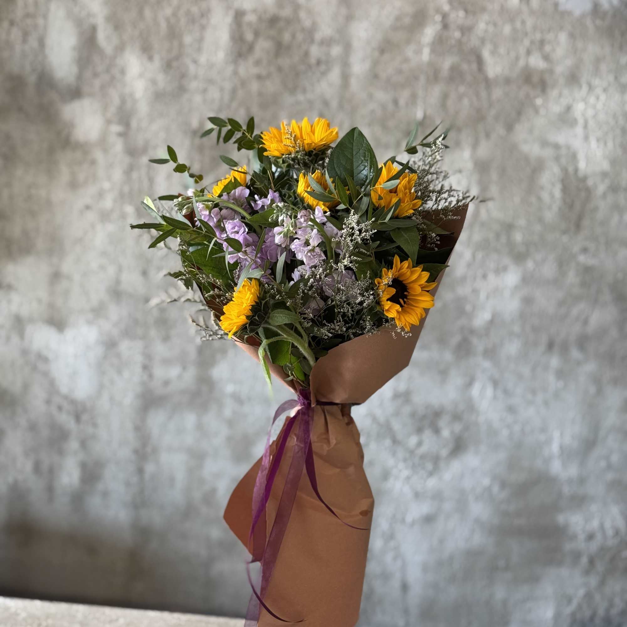 Bouquet of yellow sunflowers and lavender flowers wrapped in brown paper