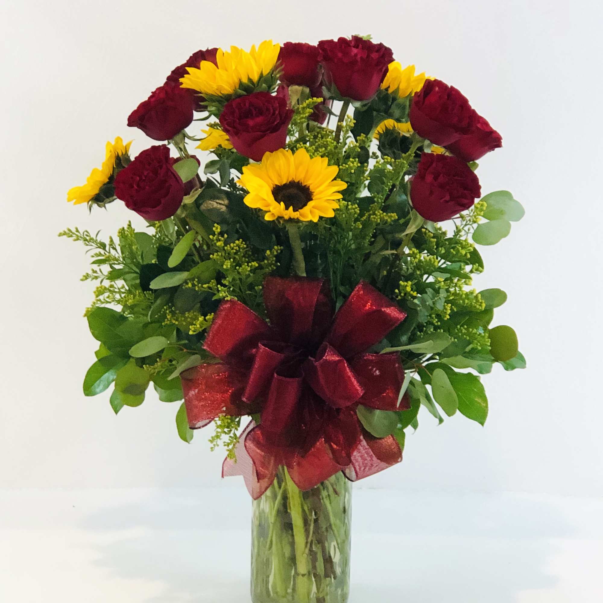 Red roses and yellow sunflowers in a glass vase with a burgundy ribbon