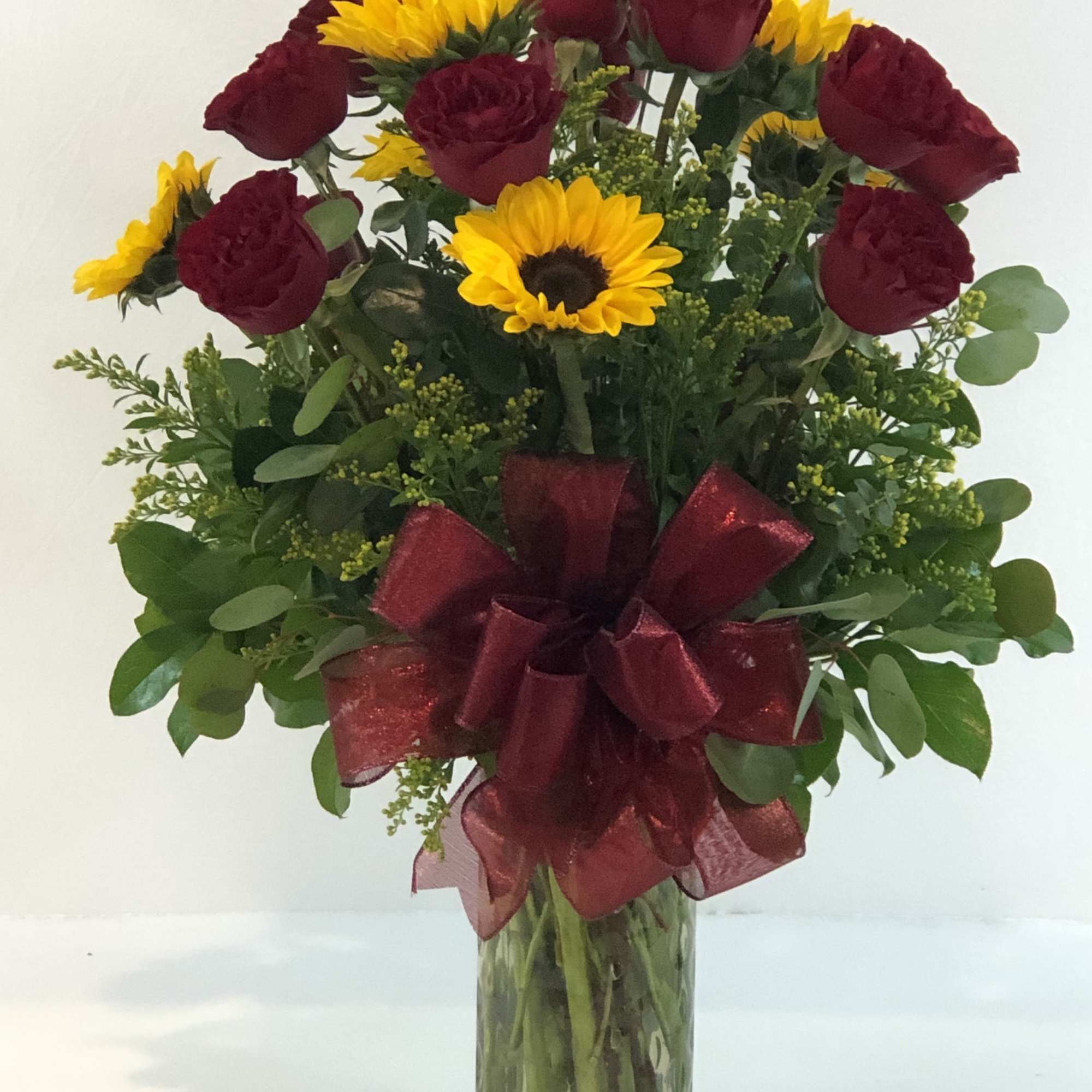 Bouquet of red carnations and yellow sunflowers in a glass vase with a burgundy ribbon