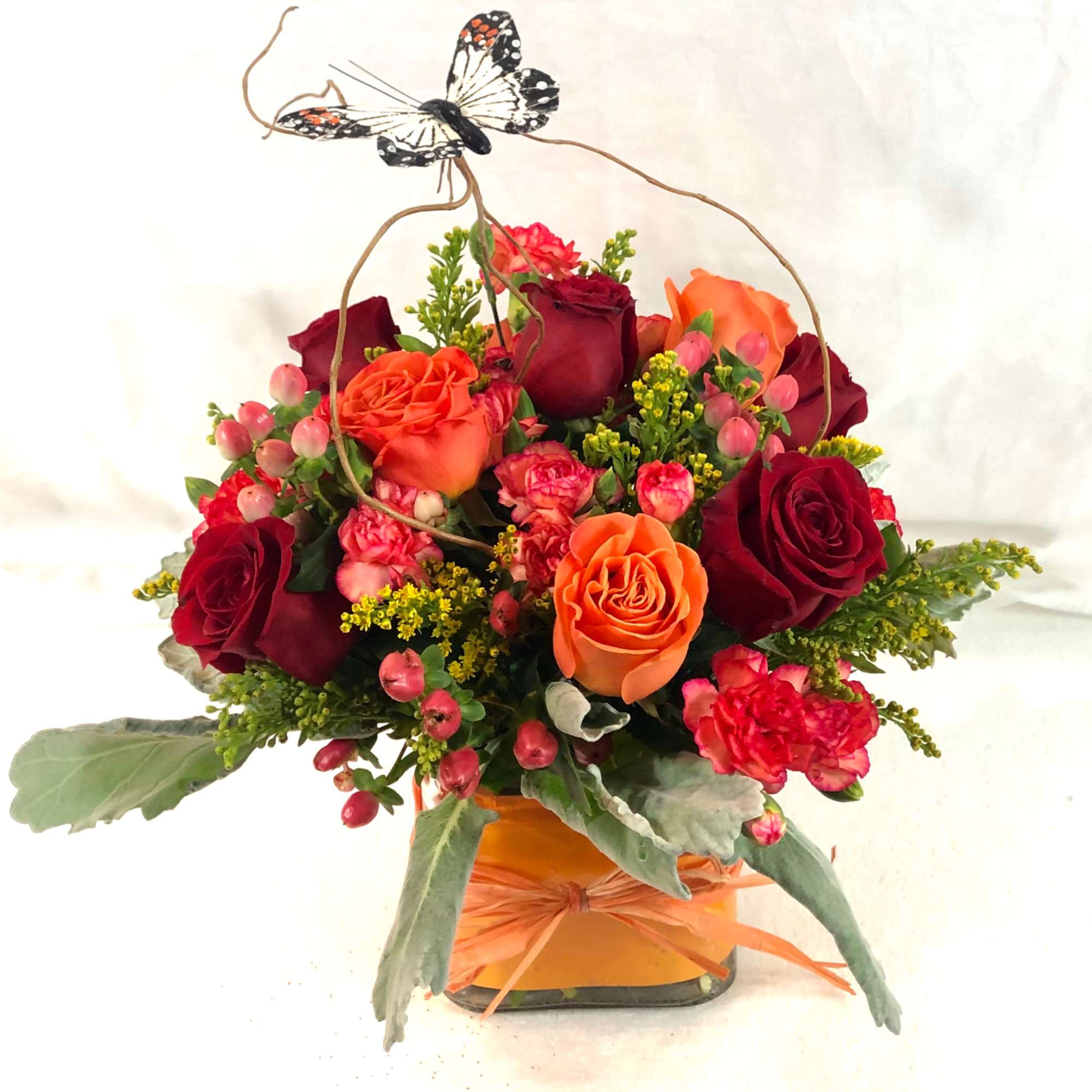 Mixed bouquet of red and orange roses in a square vase with a butterfly pick