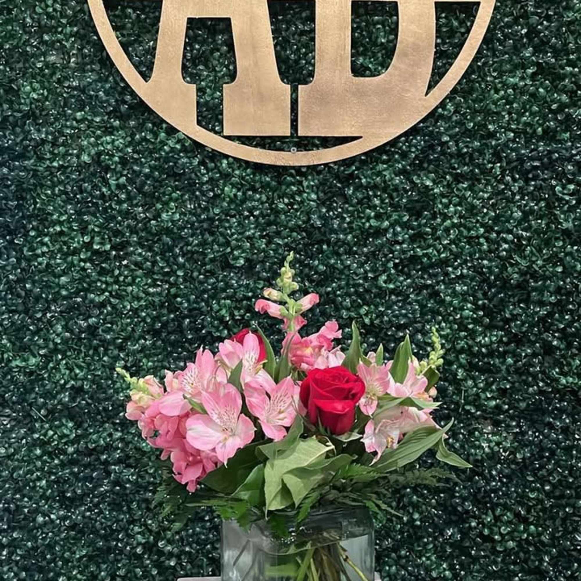 Pink flowers and a red rose in a glass vase beneath a gold "Always Beautiful" sign