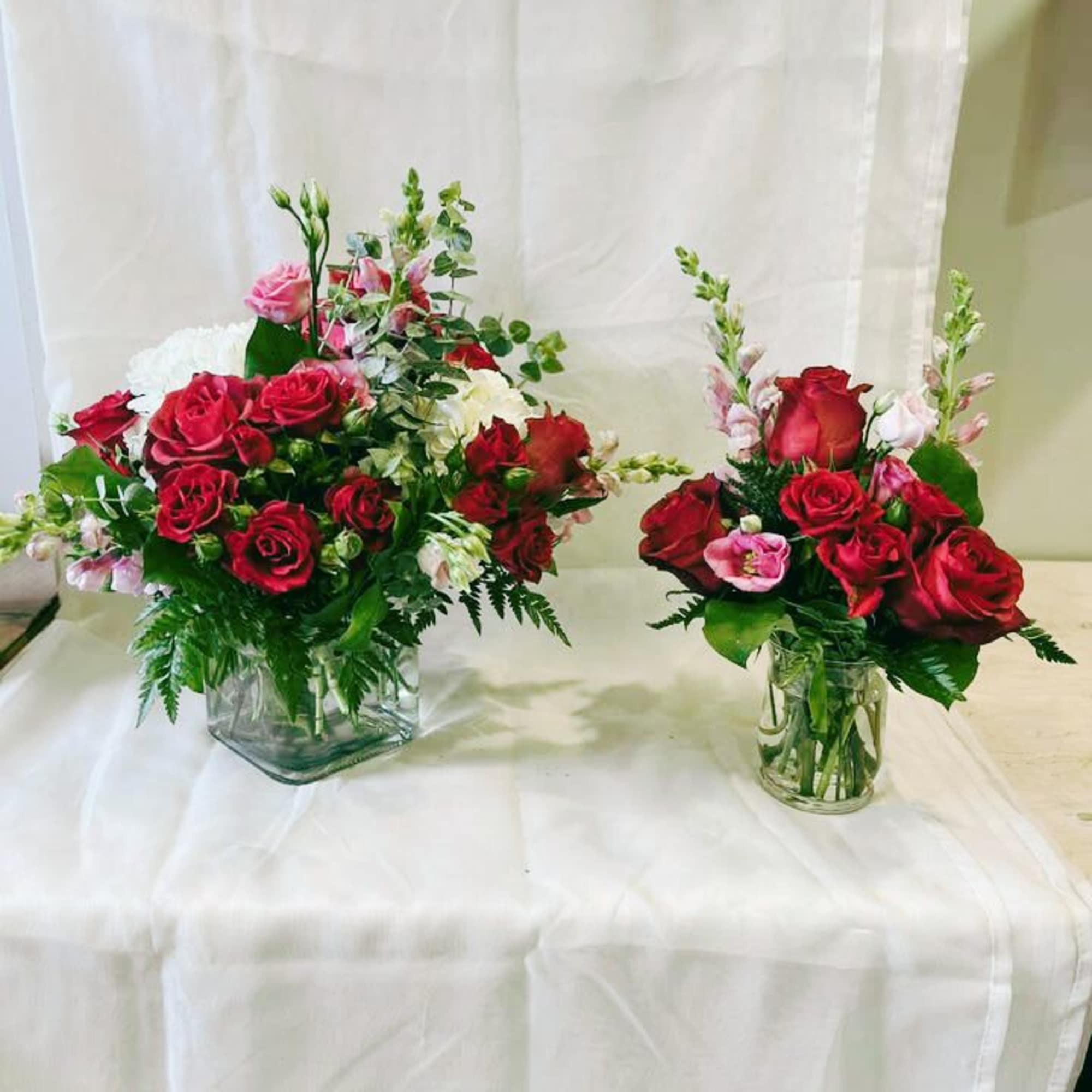 Two red rose arrangements in glass vases with pink accent flowers