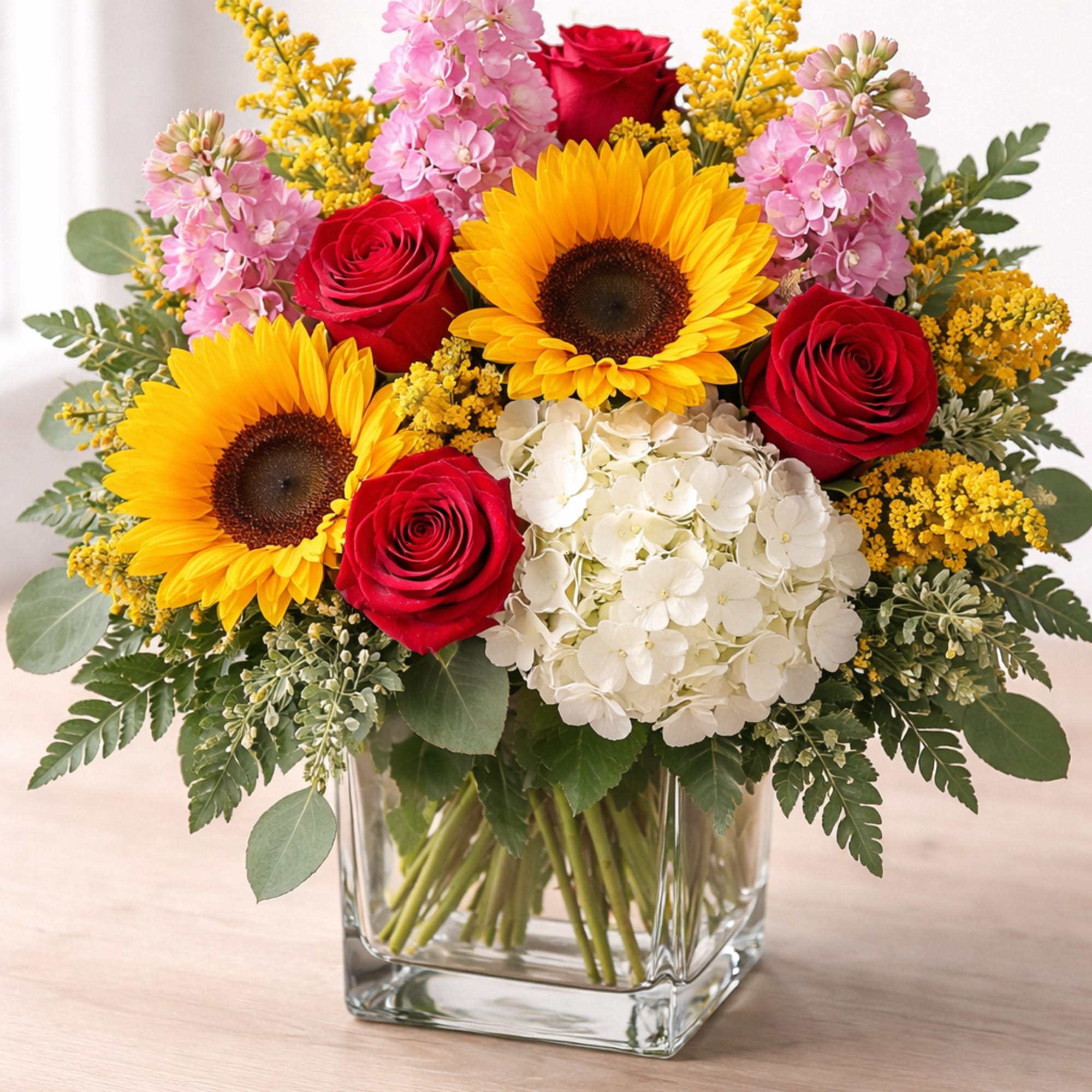 Bouquet of red roses, sunflowers, pink flowers, and white hydrangea in a glass vase