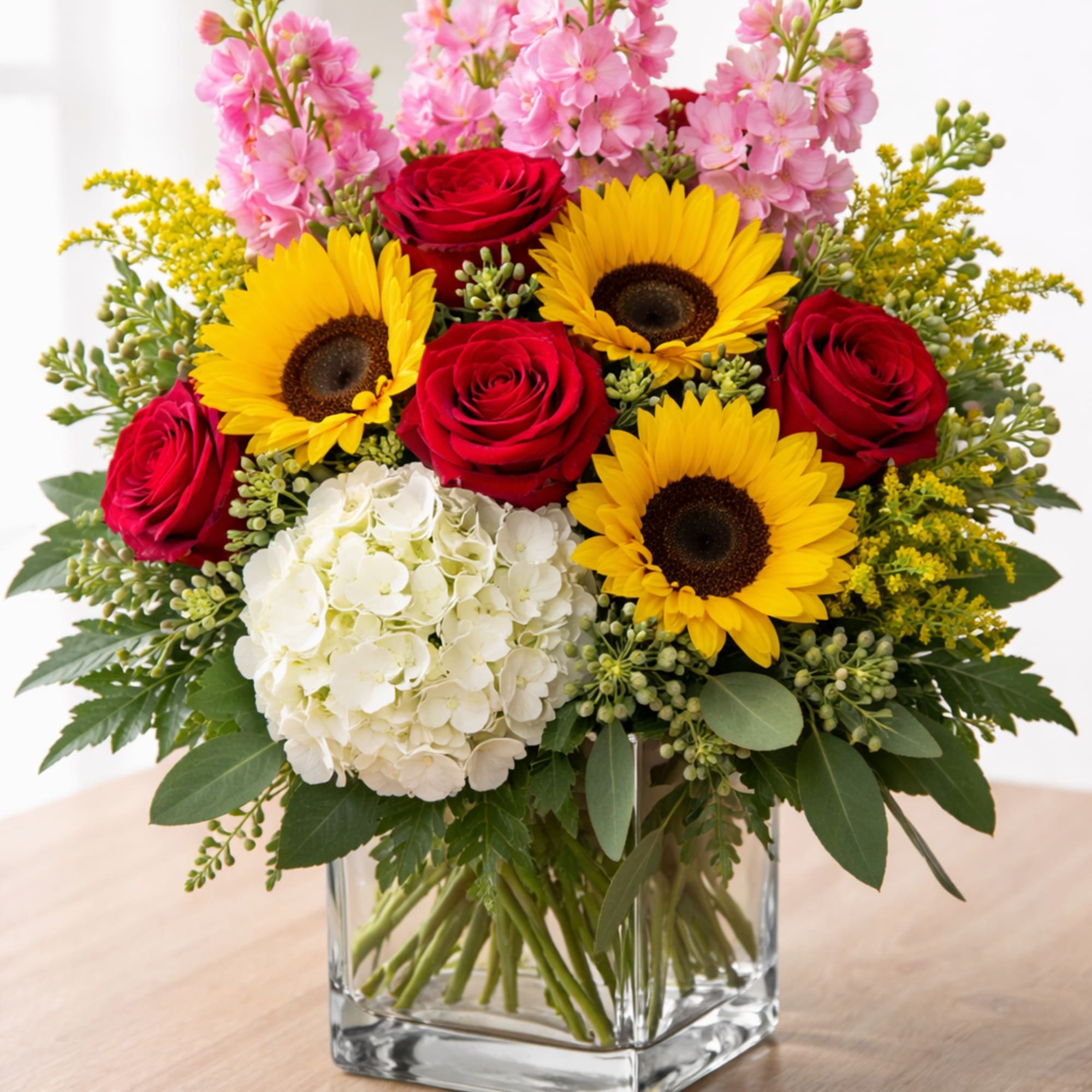 Bouquet of red roses, sunflowers, pink blooms, and white hydrangea in a glass vase
