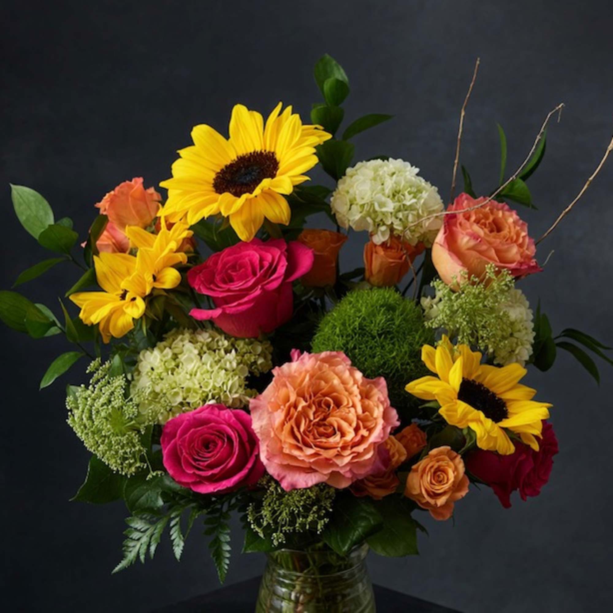 Mixed bouquet with sunflowers, roses, and hydrangeas in a glass vase