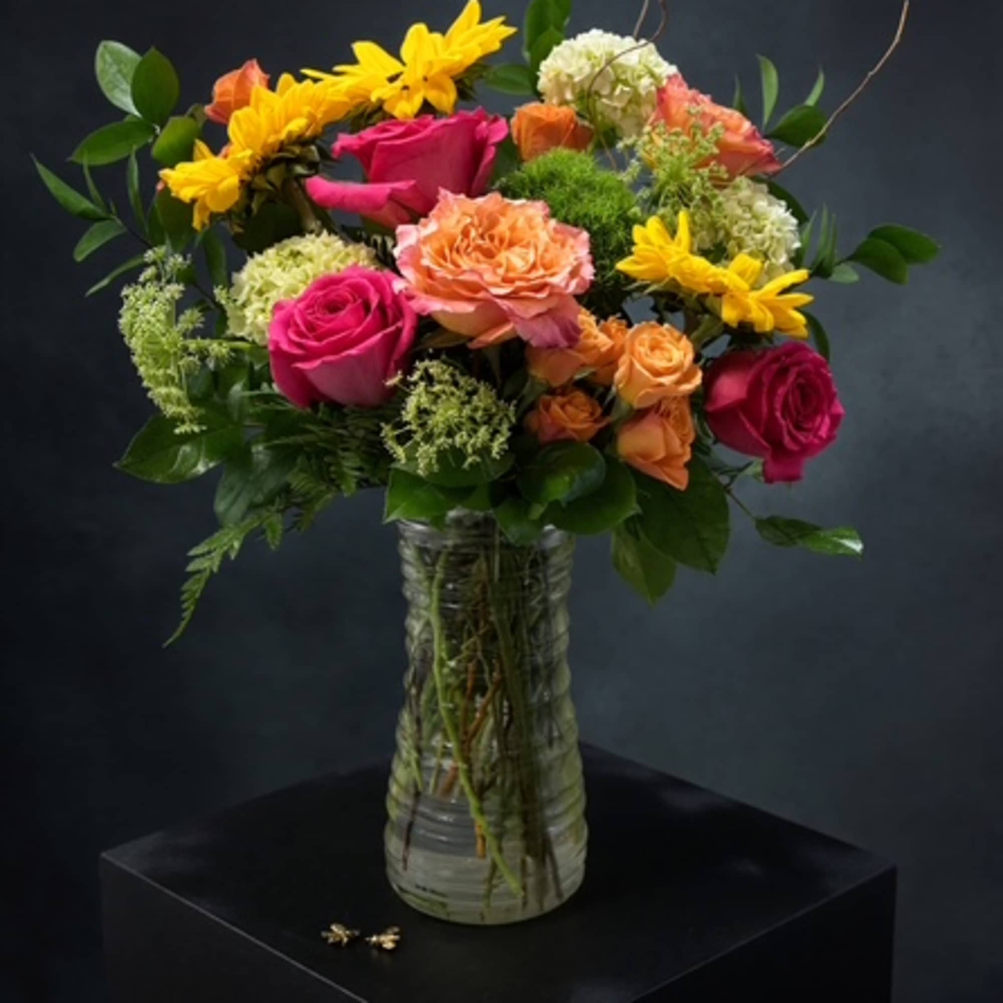 Mixed bouquet of roses, carnations, and yellow daisies in a glass vase
