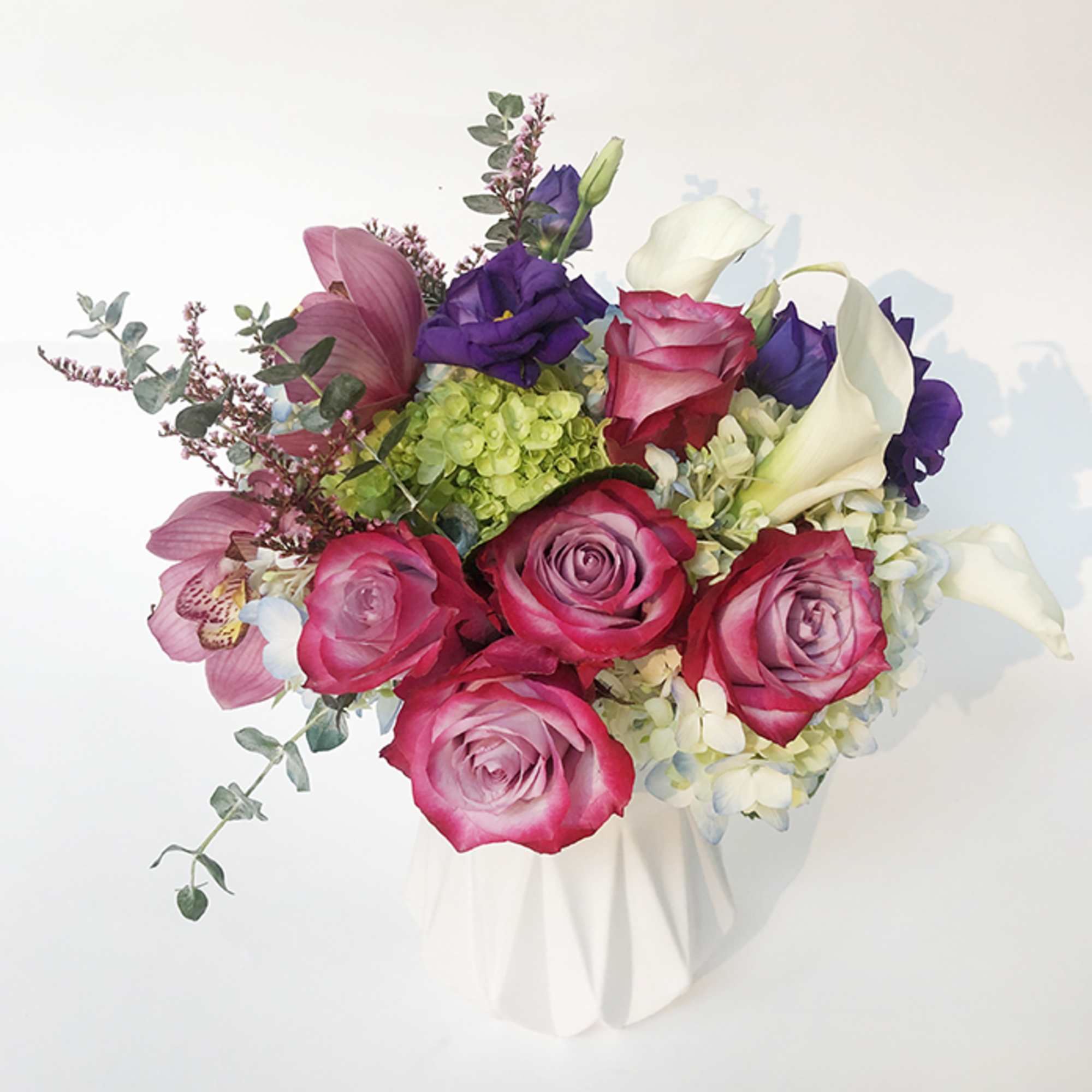 Bouquet of pink roses, purple blooms, and white calla lilies in a white wrap