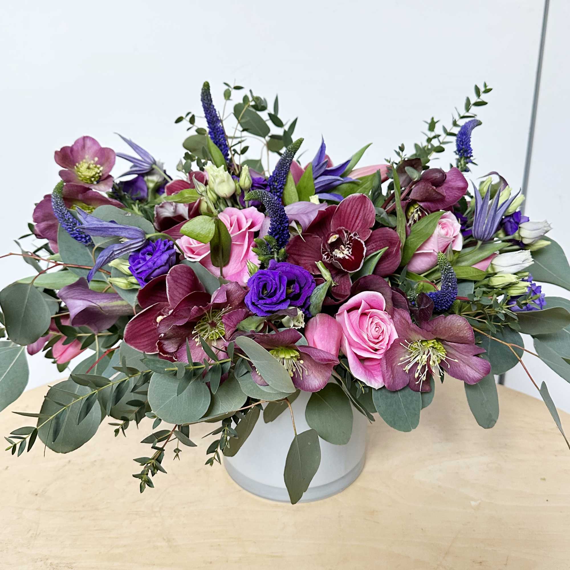 Mixed bouquet of pink, purple, and burgundy flowers in a white vase