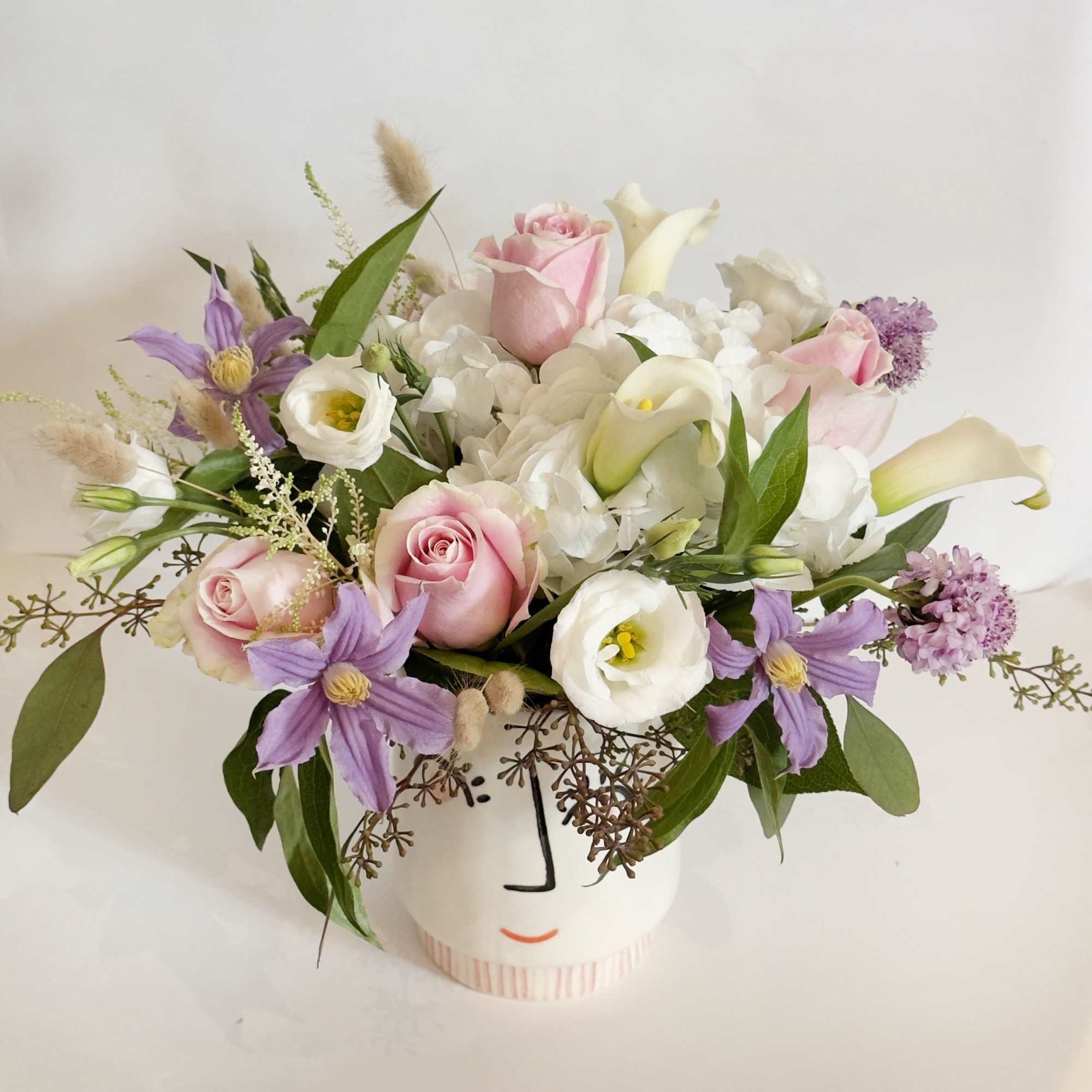 Pink roses and white calla lilies in a white vase with purple flowers